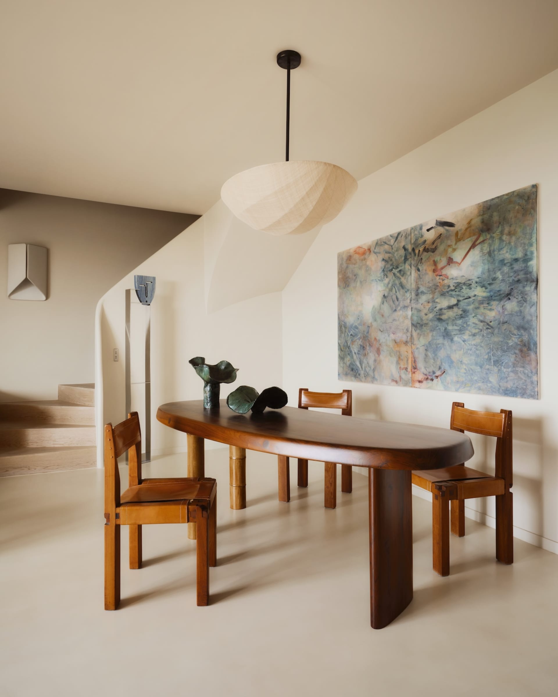 Contemporary dining area with wooden table and chairs, abstract painting, and pendant lighting.