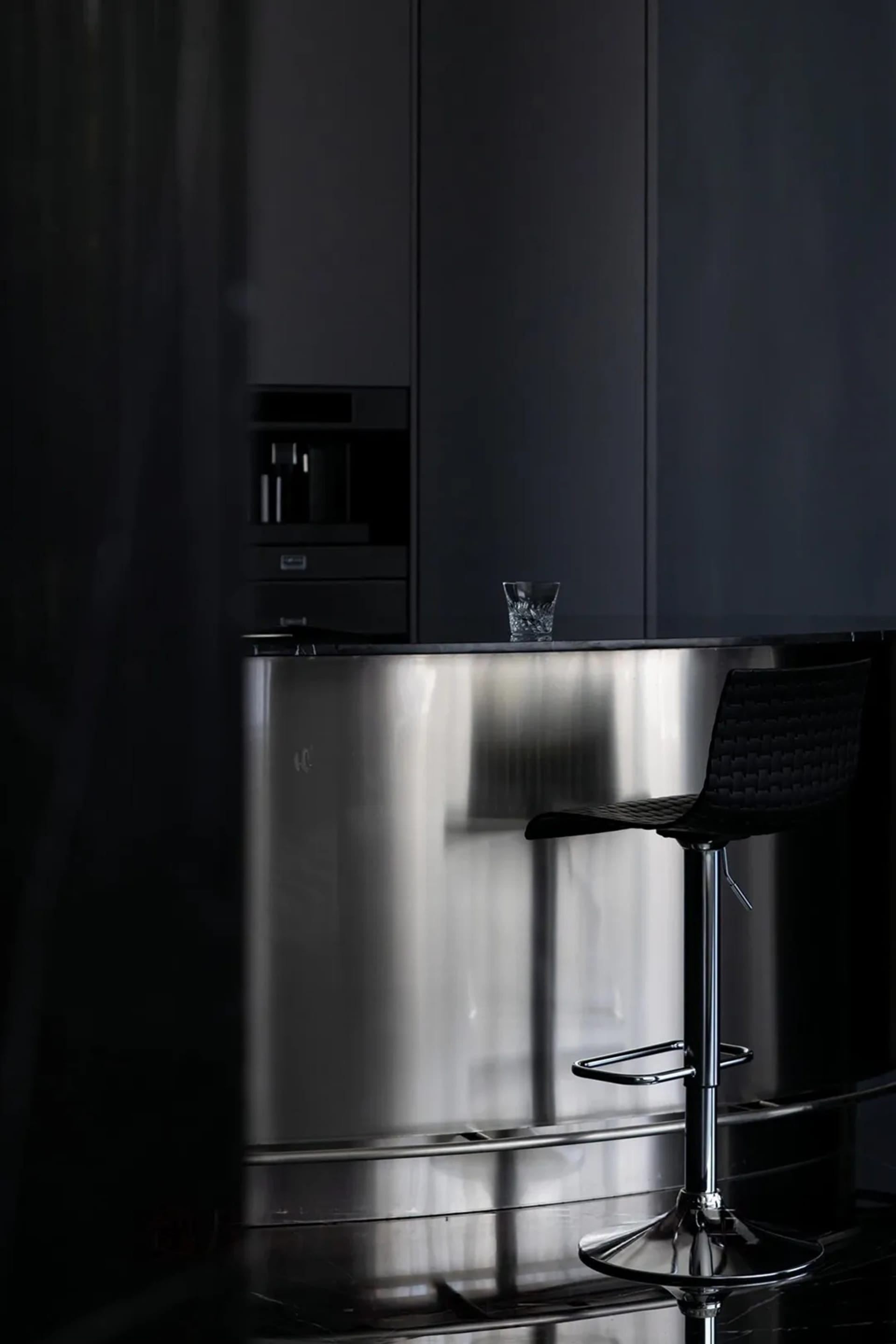 Modern minimalist kitchen with stainless steel island and black stools.