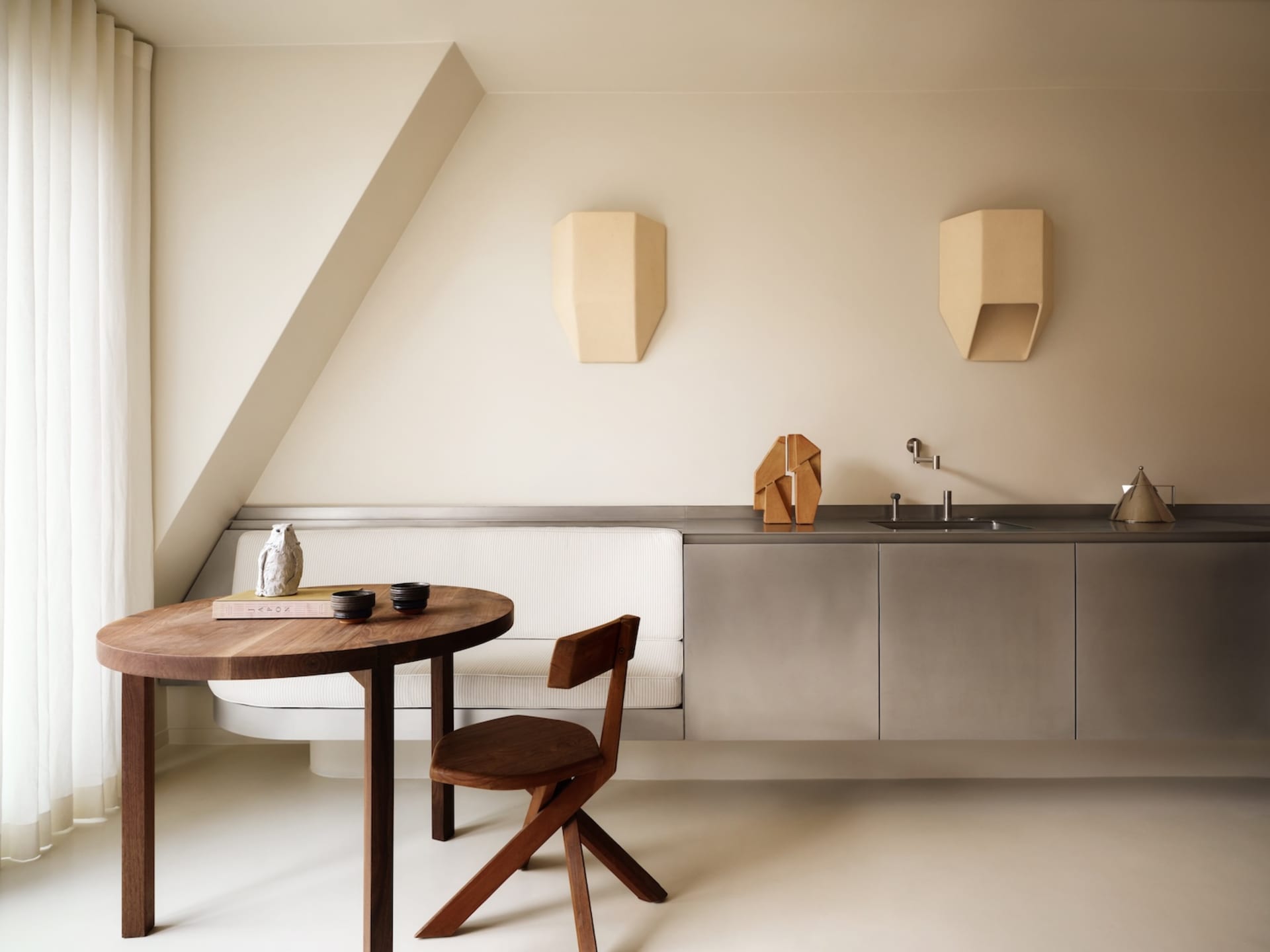 Modern minimalist kitchen with metallic cabinets, white countertop, and wooden table and chair.