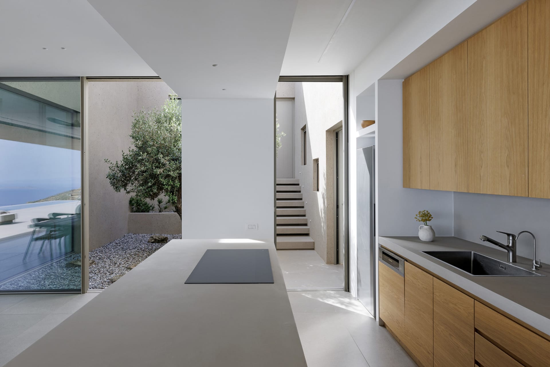 Modern minimalist residential kitchen featuring a sleek black countertop with a built-in stove, wooden cabinets, and a view o