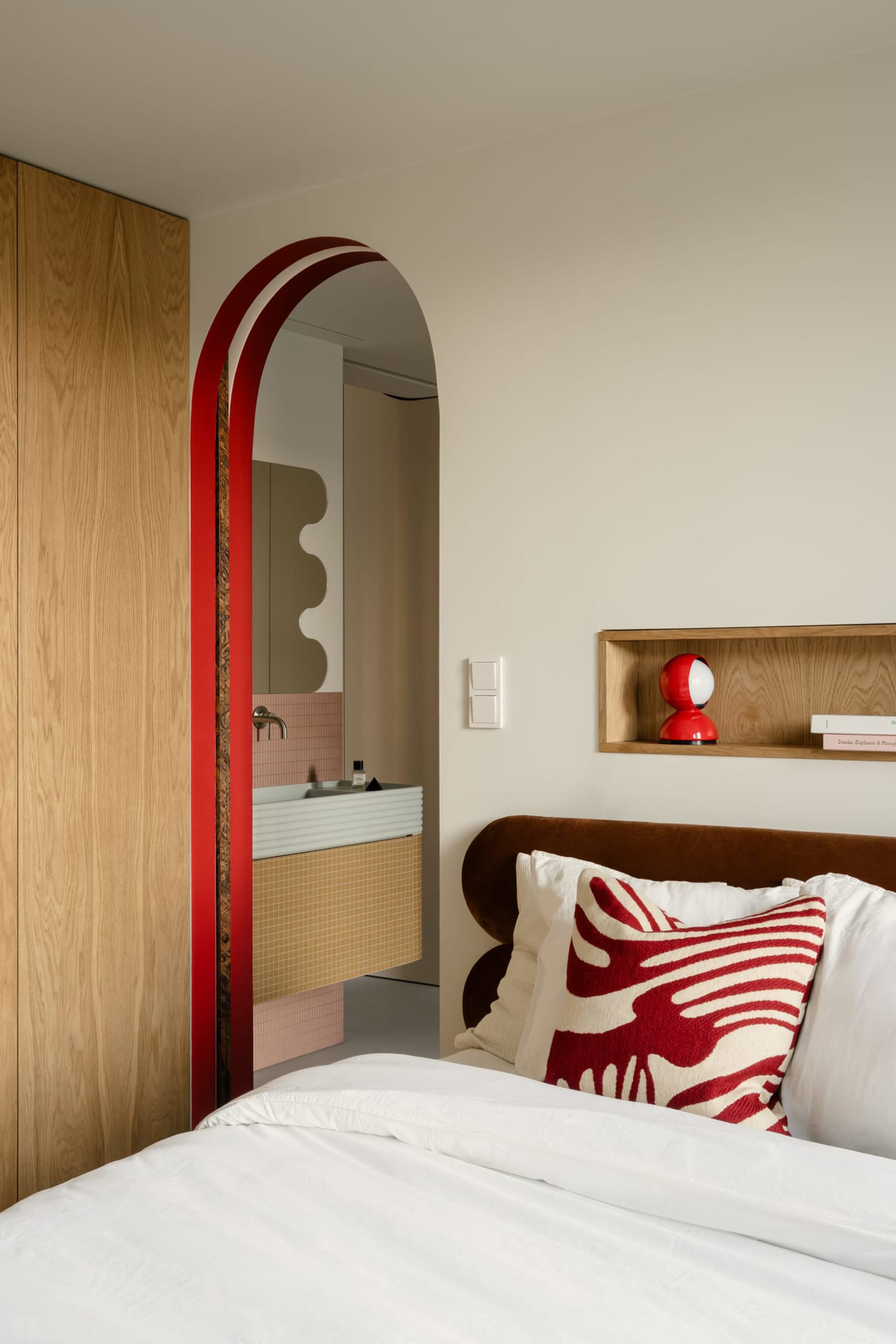 Contemporary bedroom featuring light wooden cabinets, ceramic tiles, and a plush bed with red and white decorative pillows.