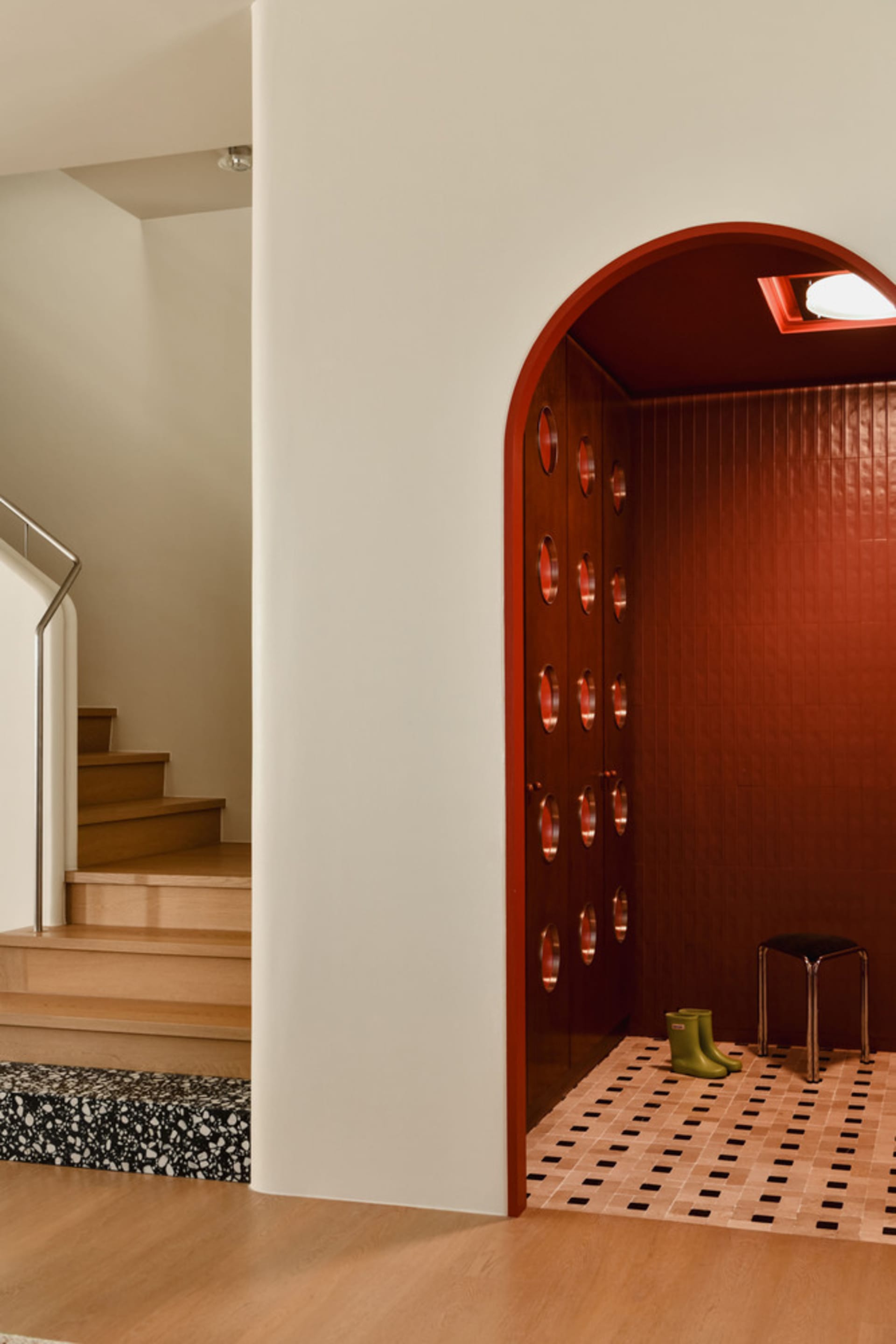 Modern entryway featuring red terrazzo tiles and a small black stool with green boots.