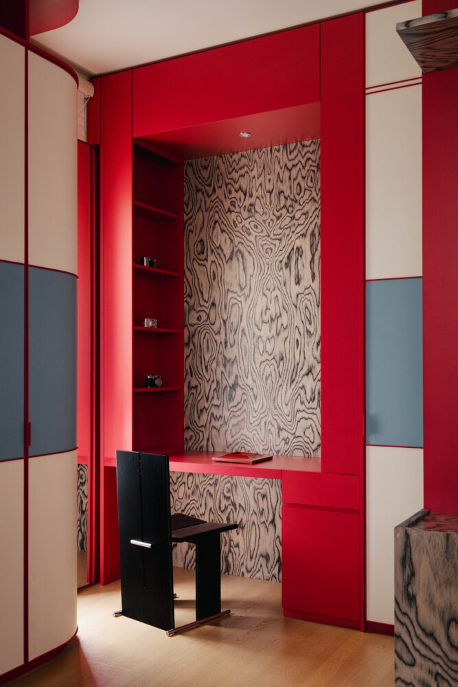 A modern home office with red walls, a black chair, and a wooden textured wall.