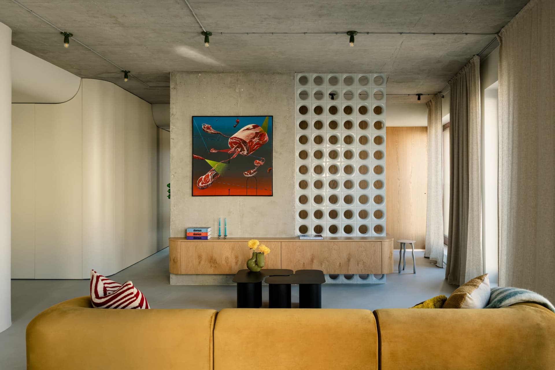 A modern living room with concrete walls, a mustard-colored sofa, and a unique wall art piece.