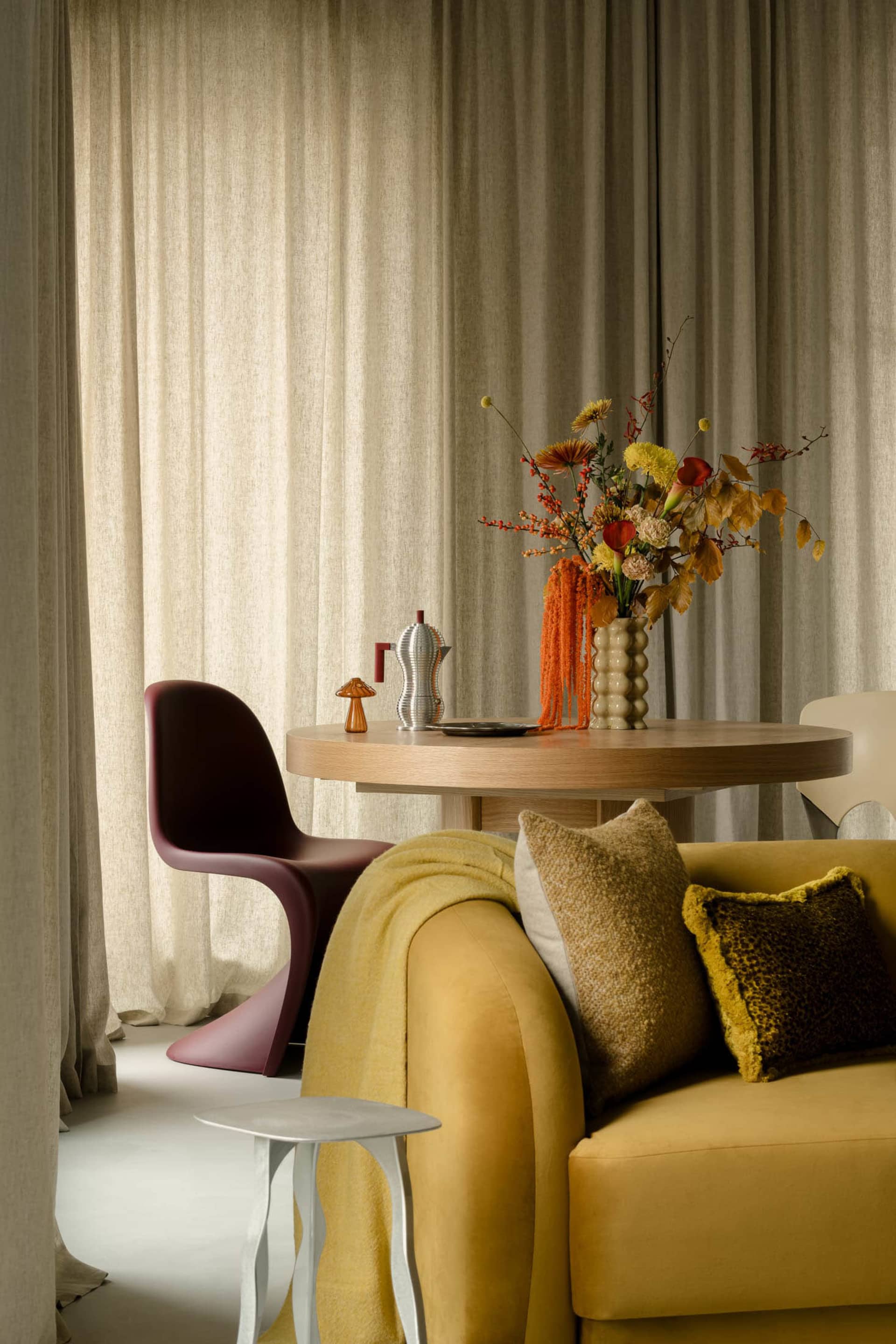 A modern sofa upholstered in mustard yellow fabric, adorned with patterned and solid throw pillows, and draped with a cozy bl