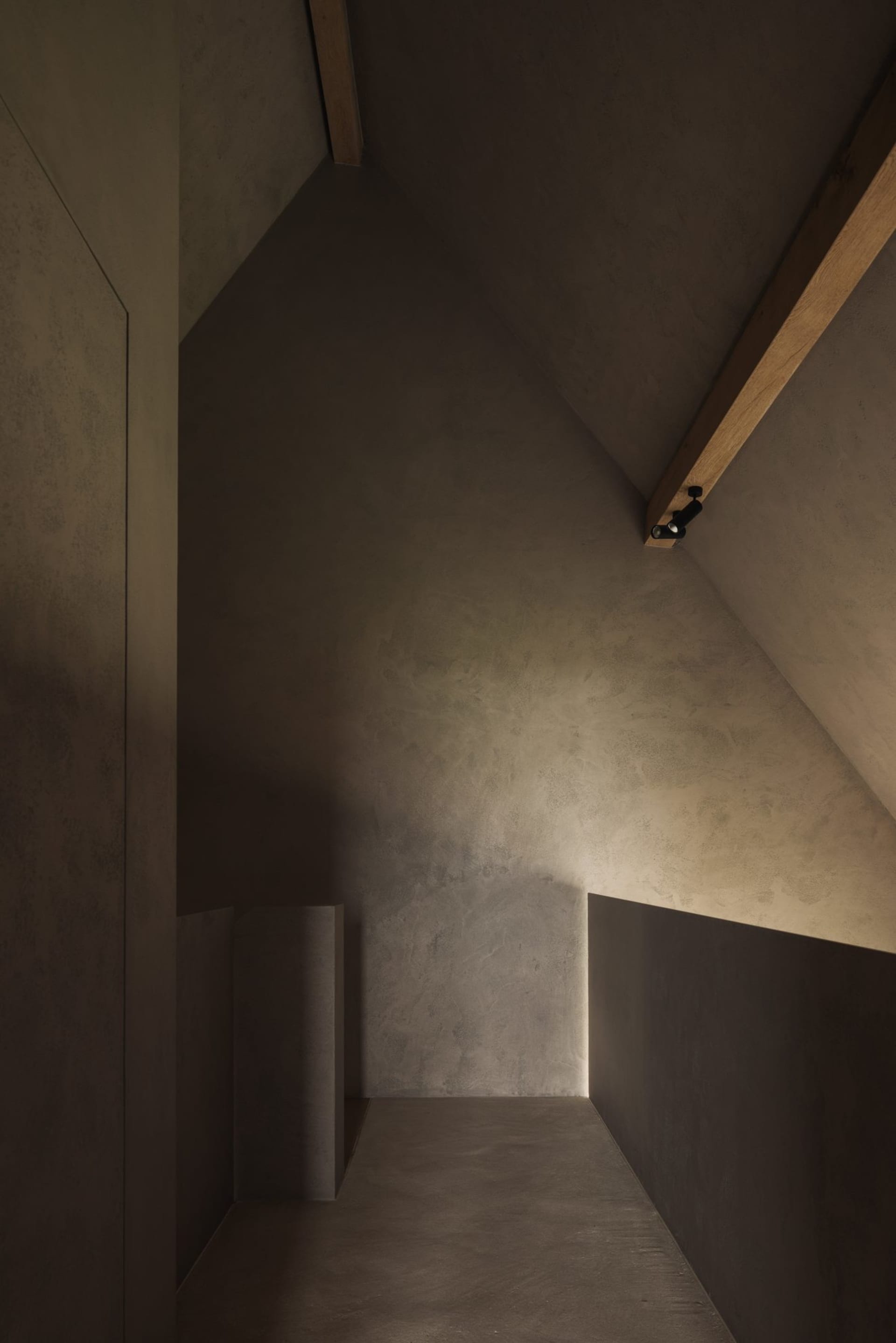A minimalist stairwell with concrete walls and floor, illuminated by a single spotlight.