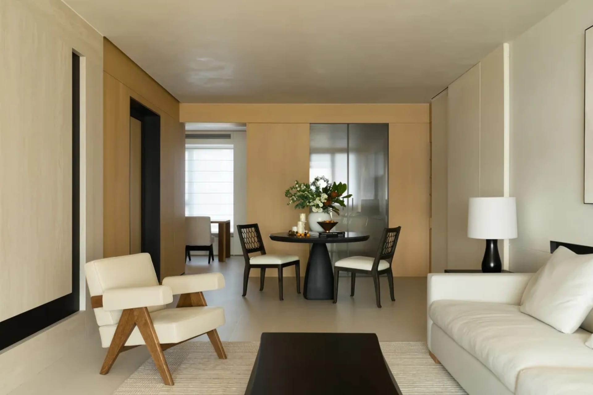 Modern minimalist living room featuring a white leather sofa, black coffee table, and wooden armchair with glass vase and bla