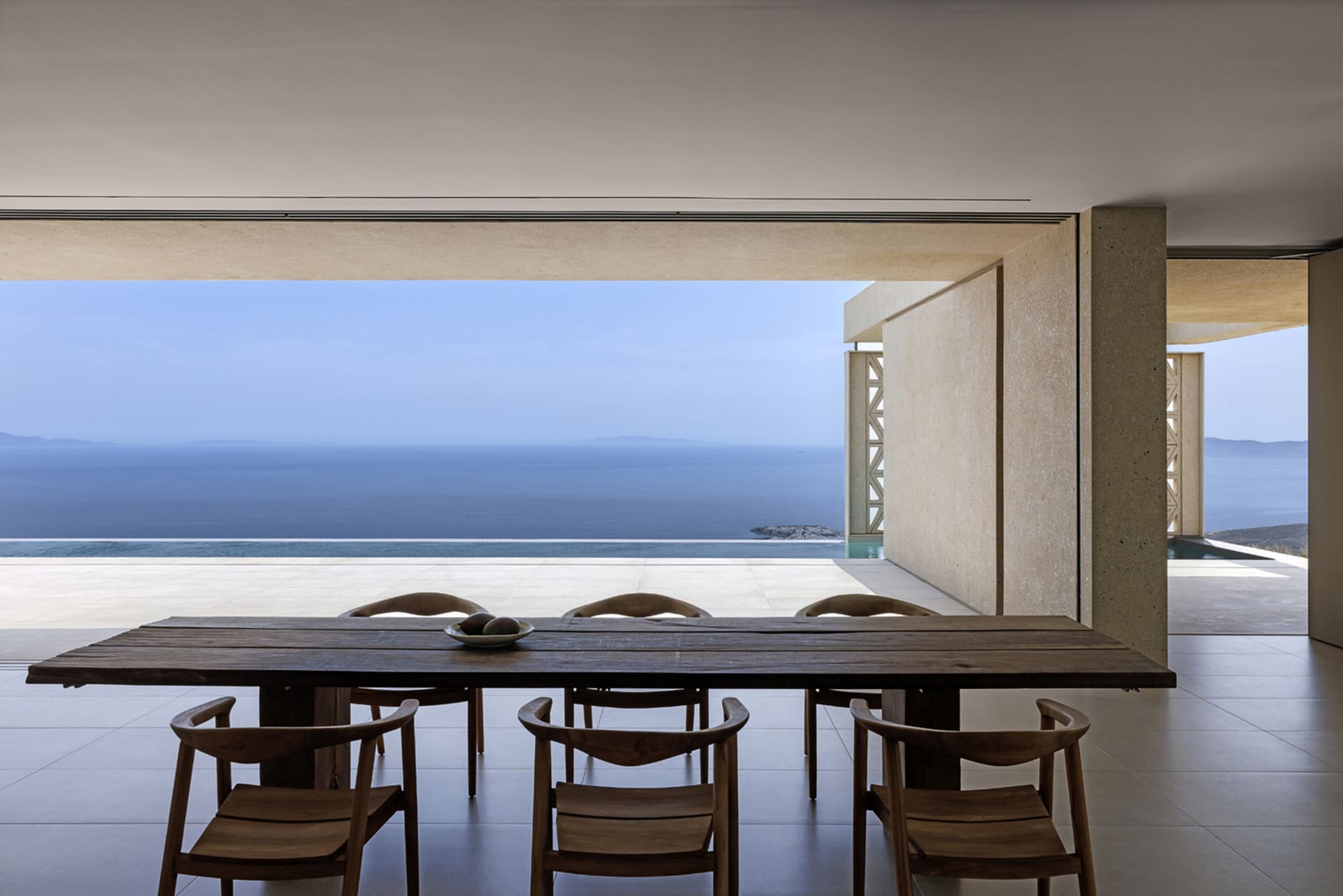 A modern residential interior with a natural wood dining table and chairs overlooking the sea.