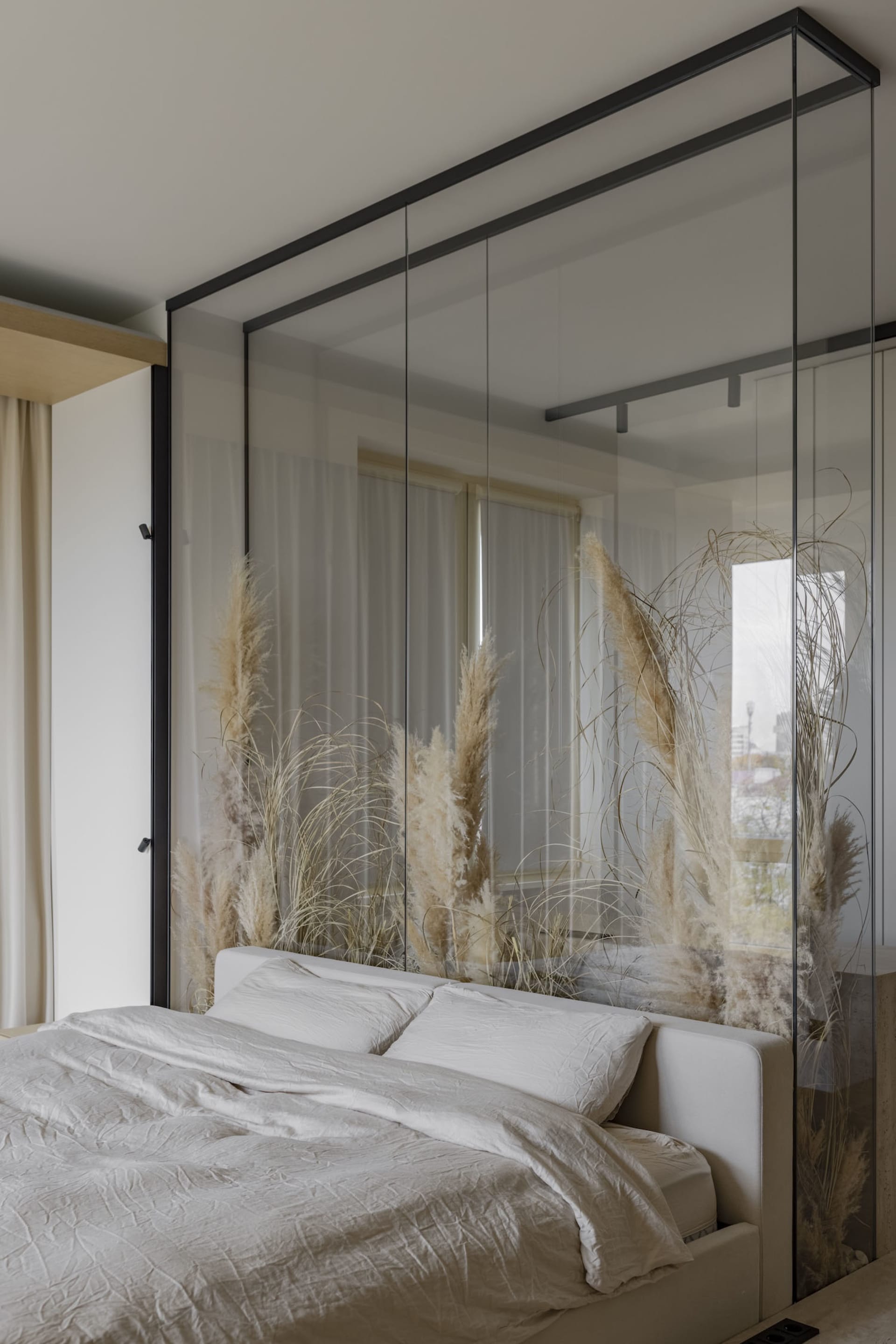 Bedroom featuring a bed with white bedding and pampas grass, behind a glass partition.