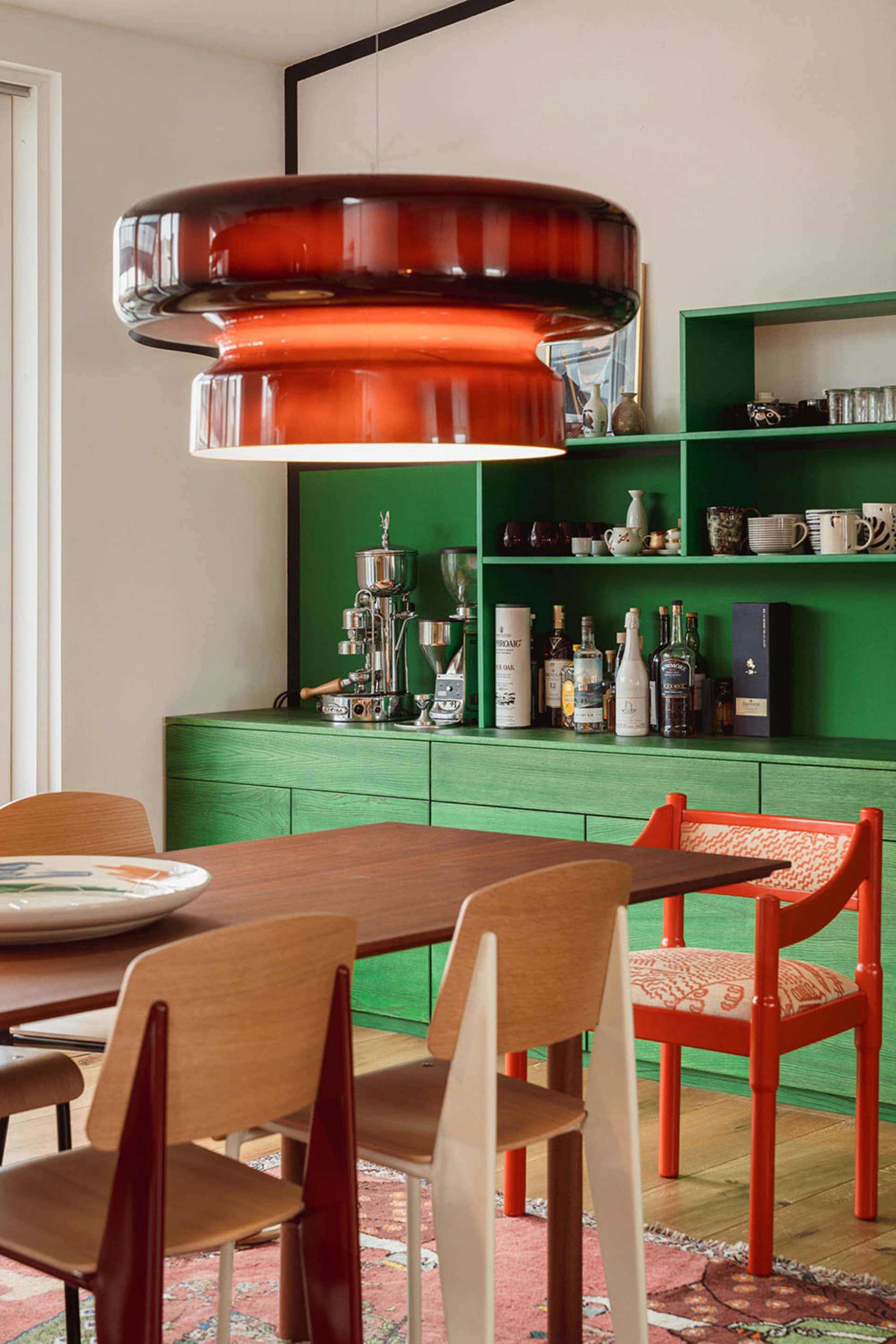 Modern interior design featuring wooden dining table, green shelves, and red chairs