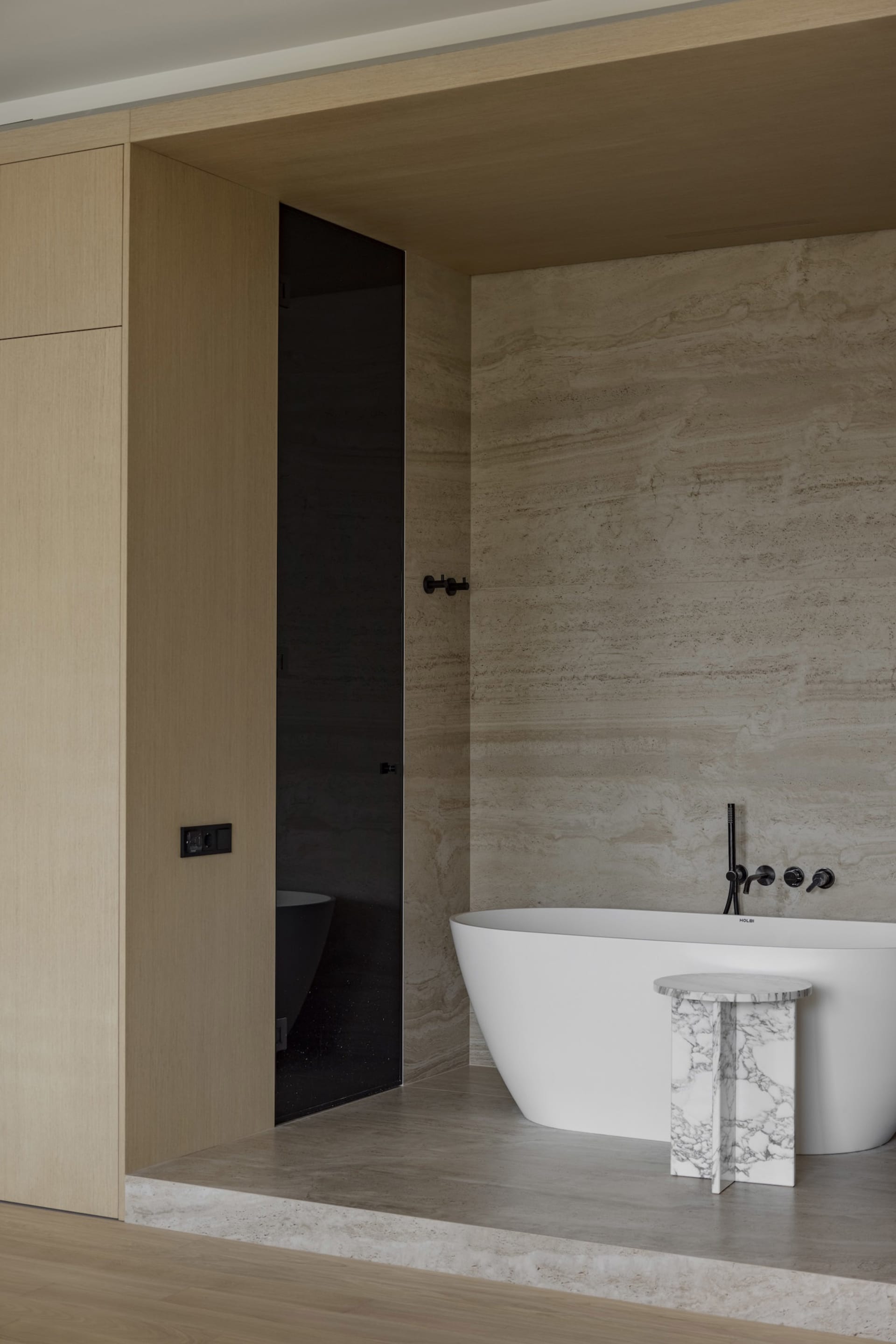 Modern minimalist bathroom featuring a white freestanding bathtub with marble accents and concrete floor.
