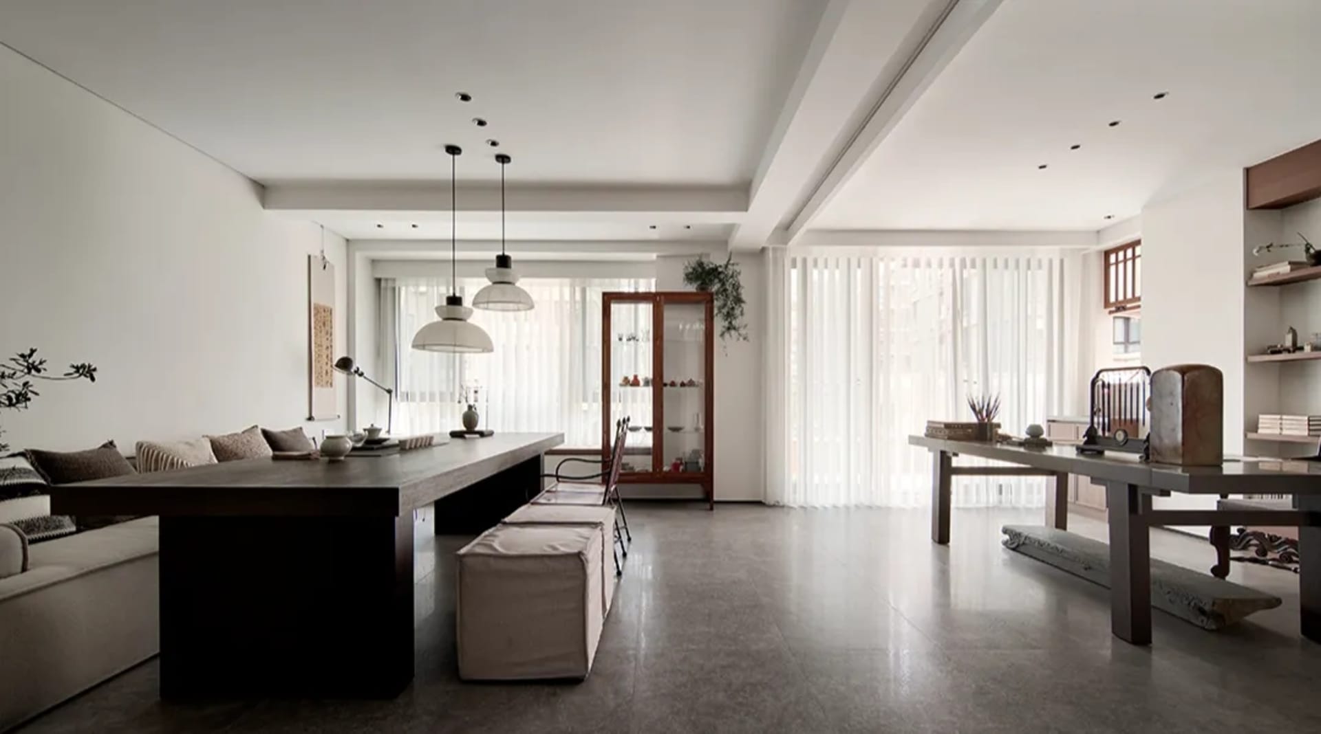 A modern minimalist living room with concrete and wood furniture, large windows, and a low-slung sofa.