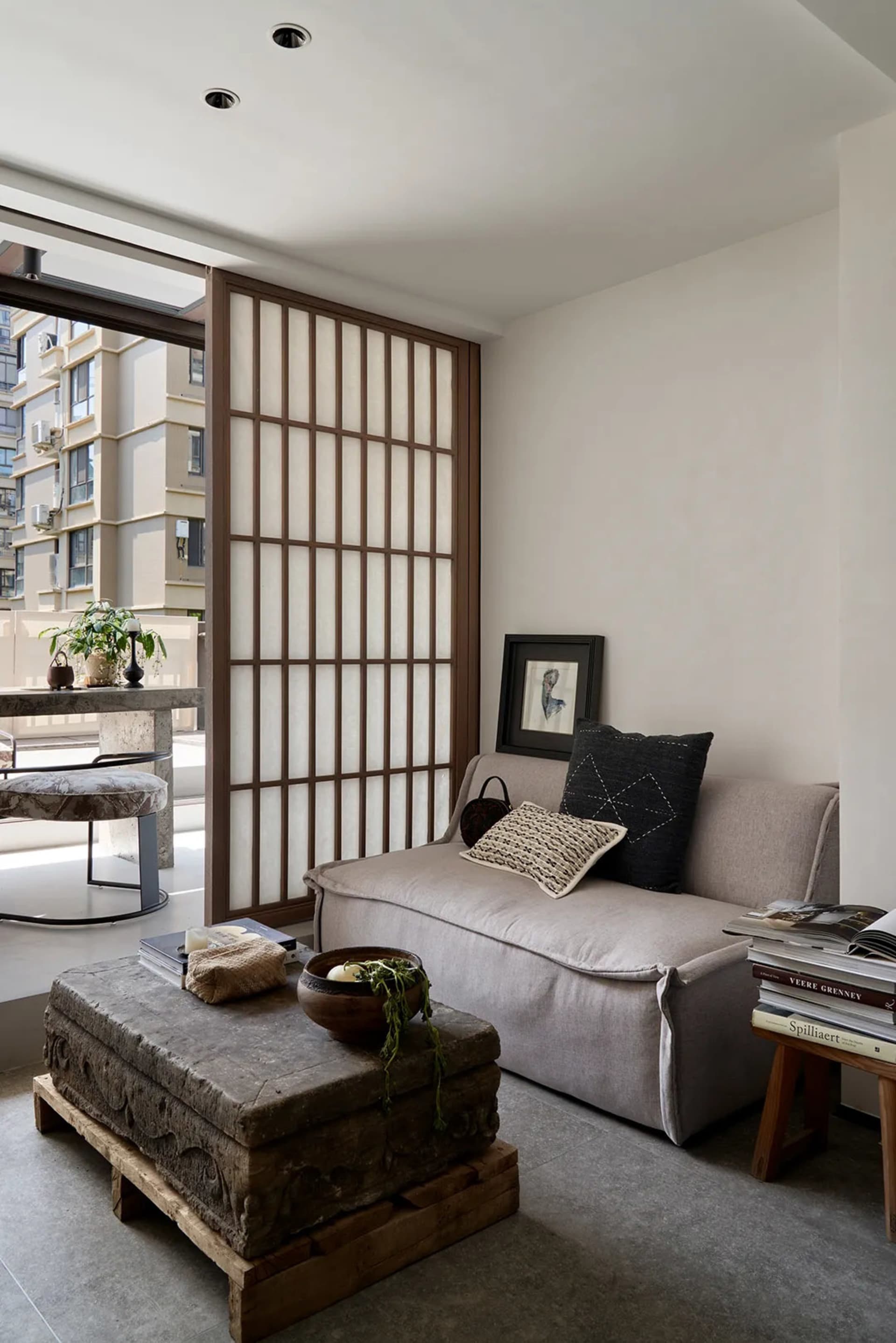 A modern living room featuring a concrete coffee table on wooden pallets, a minimalist sofa with cushions, and a wooden scree