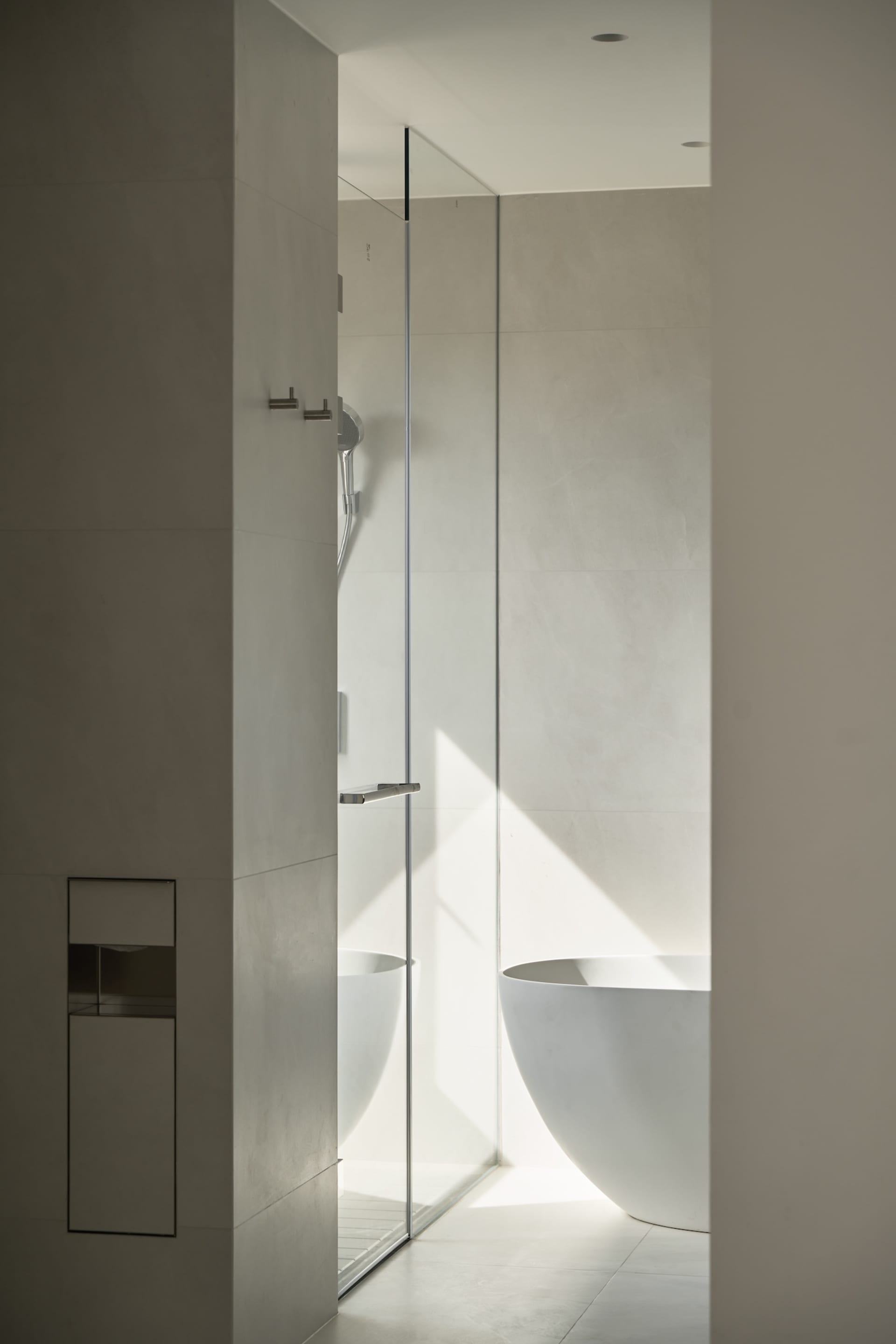 A minimalist bathroom with a freestanding white bathtub, concrete walls, and glass shower enclosure.