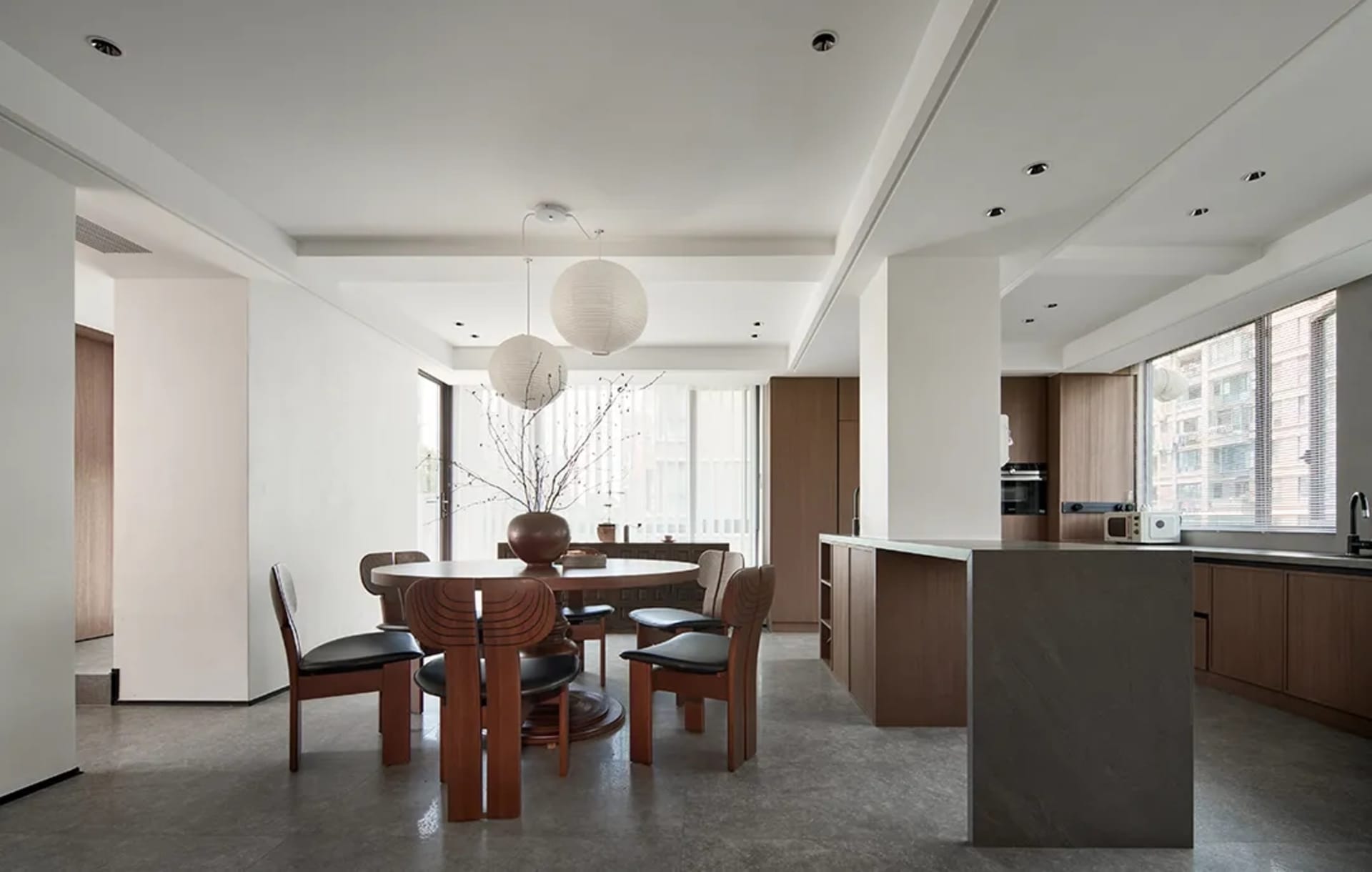 A modern residential kitchen with wood accents featuring a round dining table and chairs, a stone countertop, and a view of t