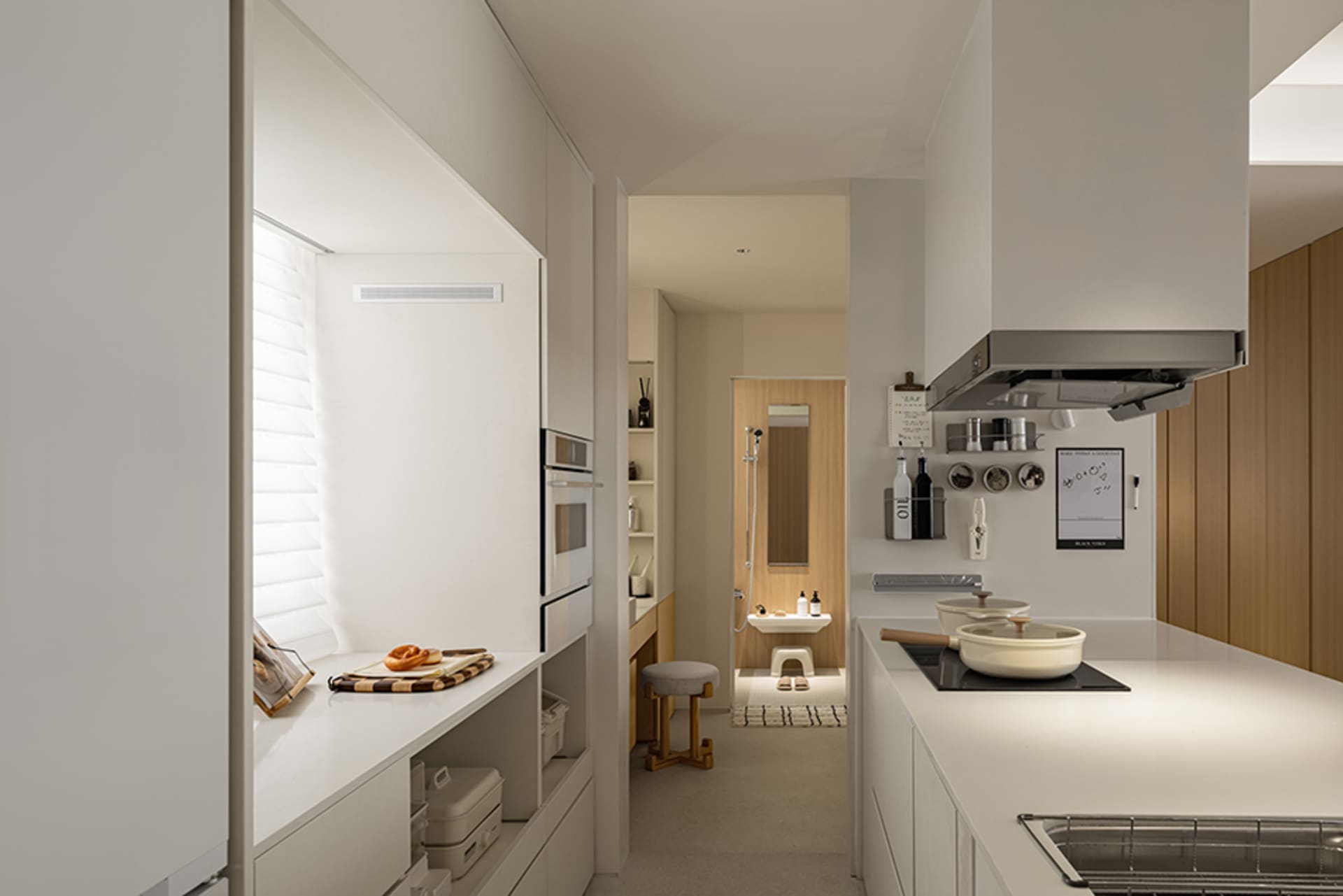 A minimalist white kitchen with wood accents, including a window with blinds, integrated appliances, and a cooktop with pots