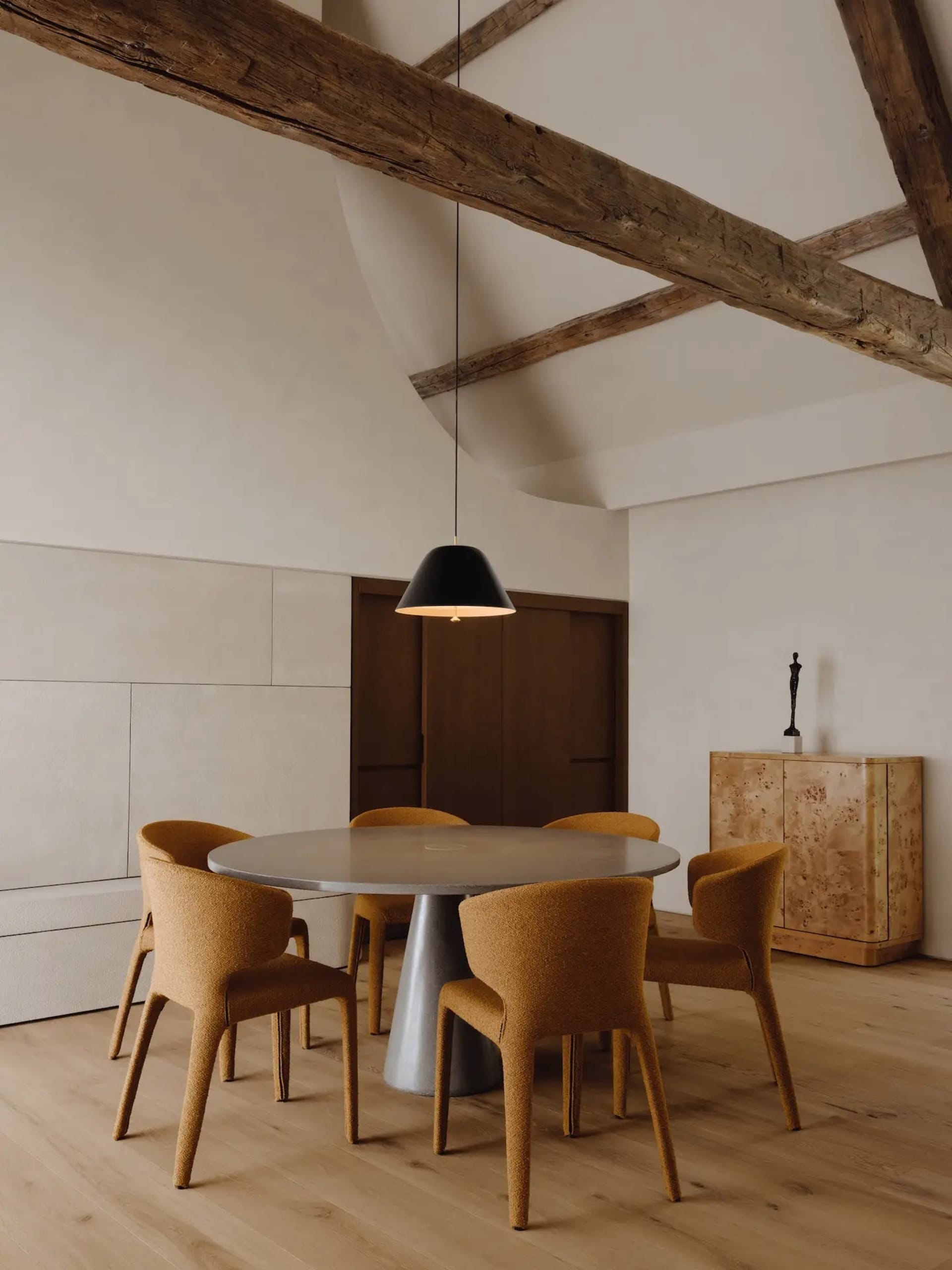 Industrial dining room with concrete table, wooden chairs, and rustic ceiling beams
