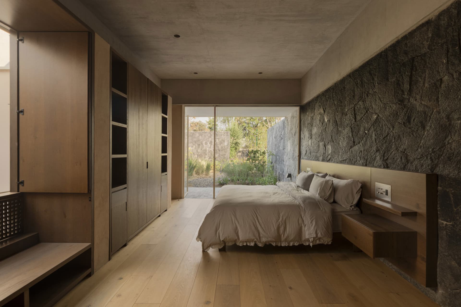 Minimalist bedroom featuring hardwood flooring and a stone wall.