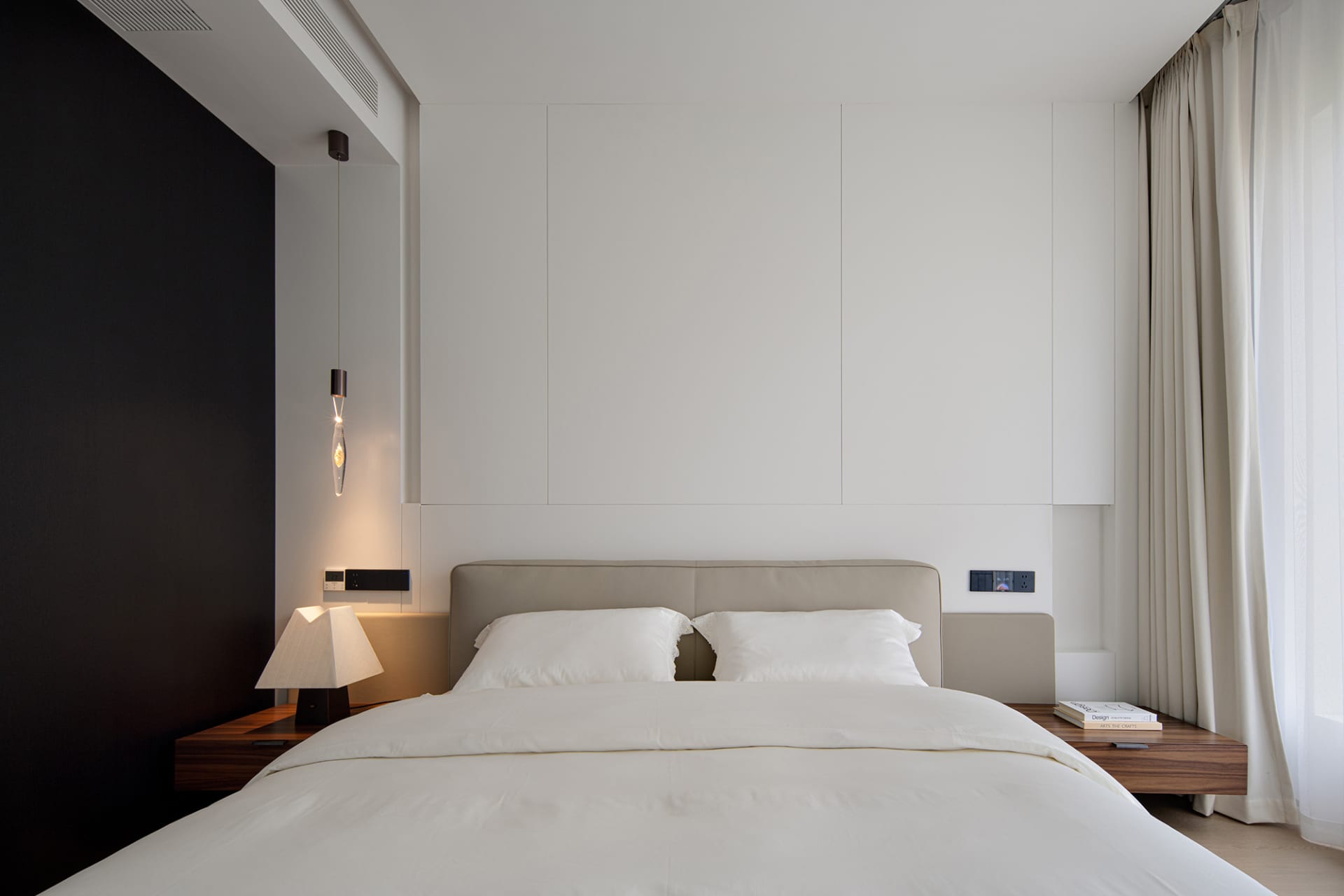 A minimalist bedroom with a bed adorned with white bedding and a hanging light fixture.