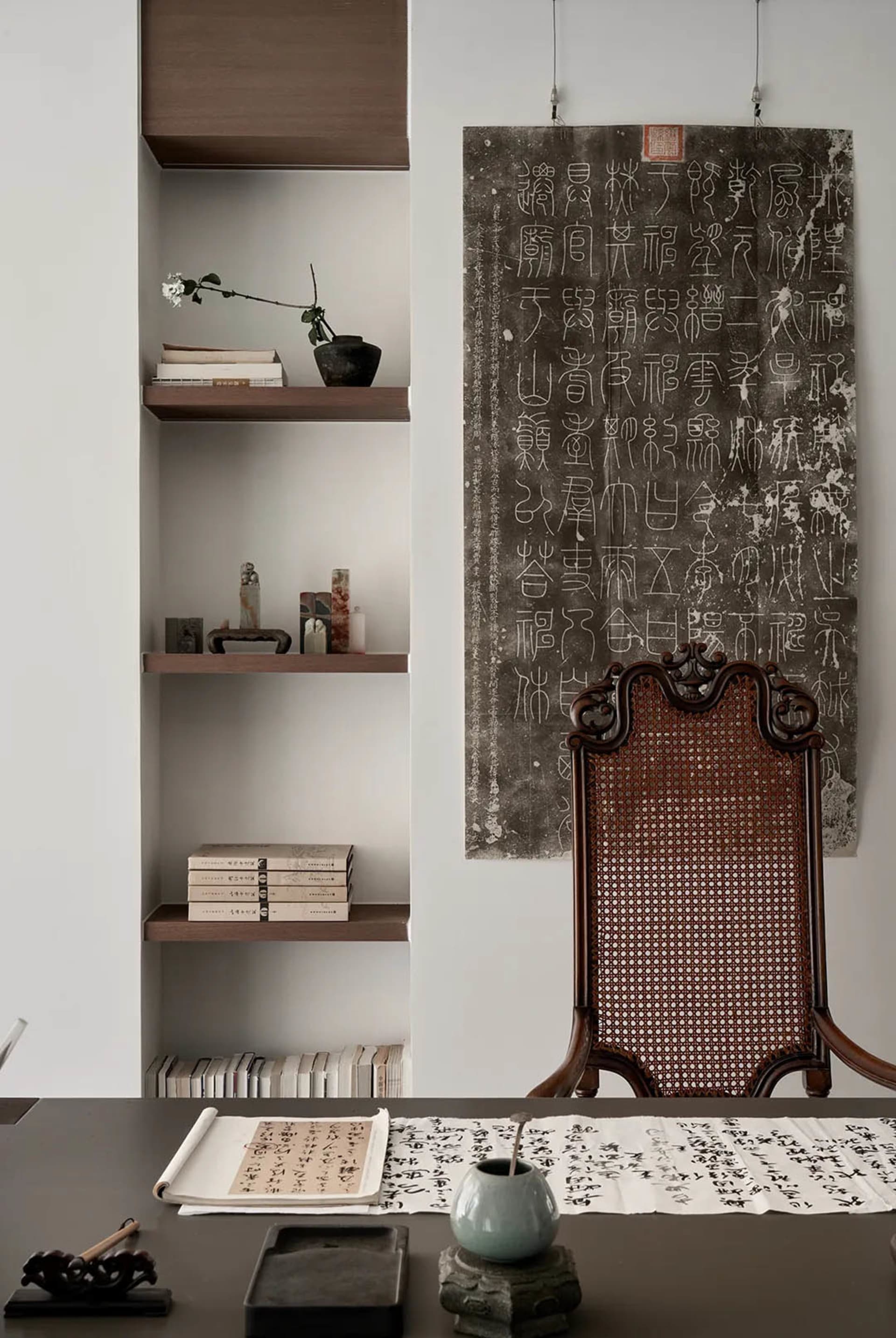 Minimalist office with wooden shelves, paper artwork, and a wicker-back chair.