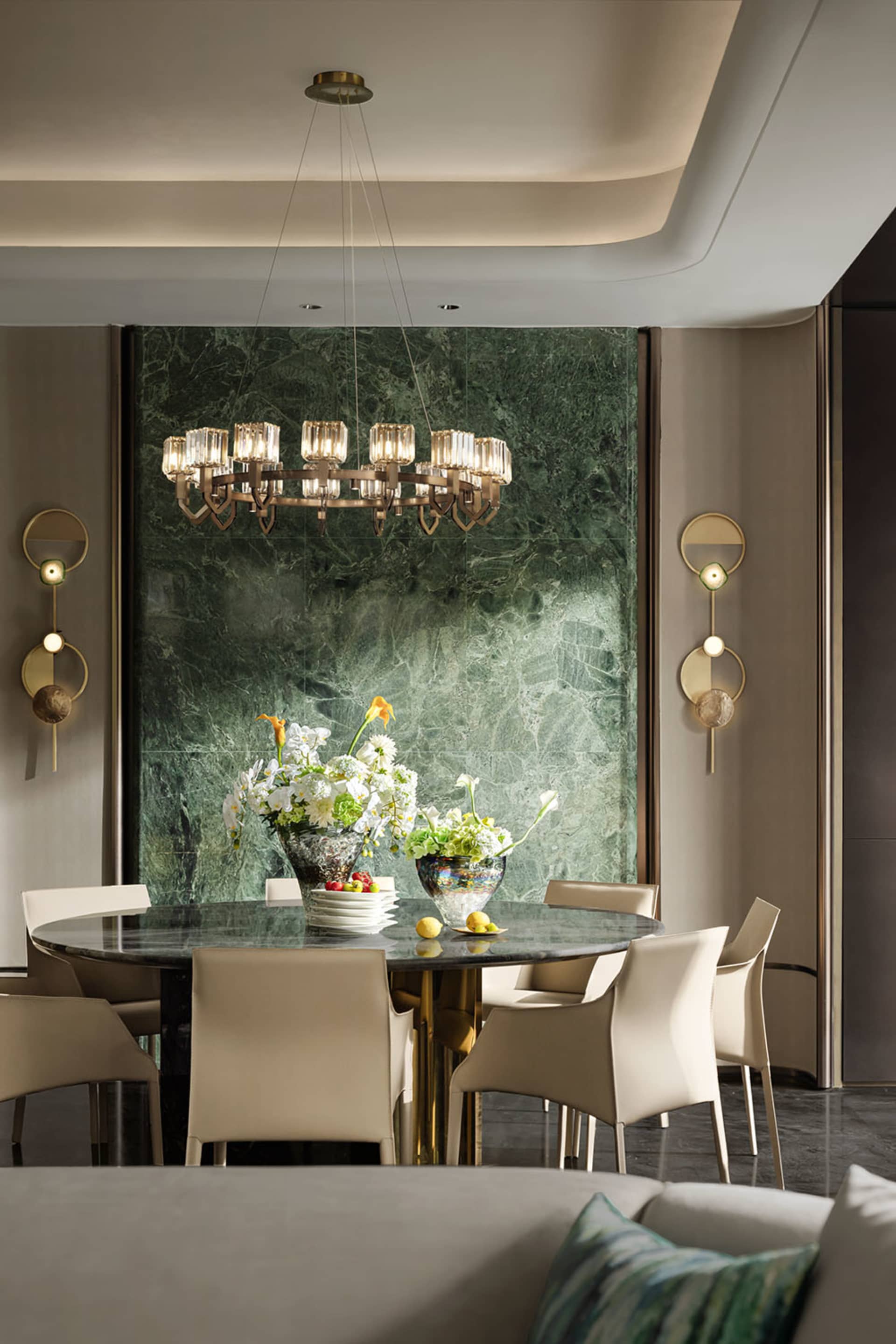 A modern luxury dining room featuring a round table, white chairs, and a chandelier hanging from the ceiling.
