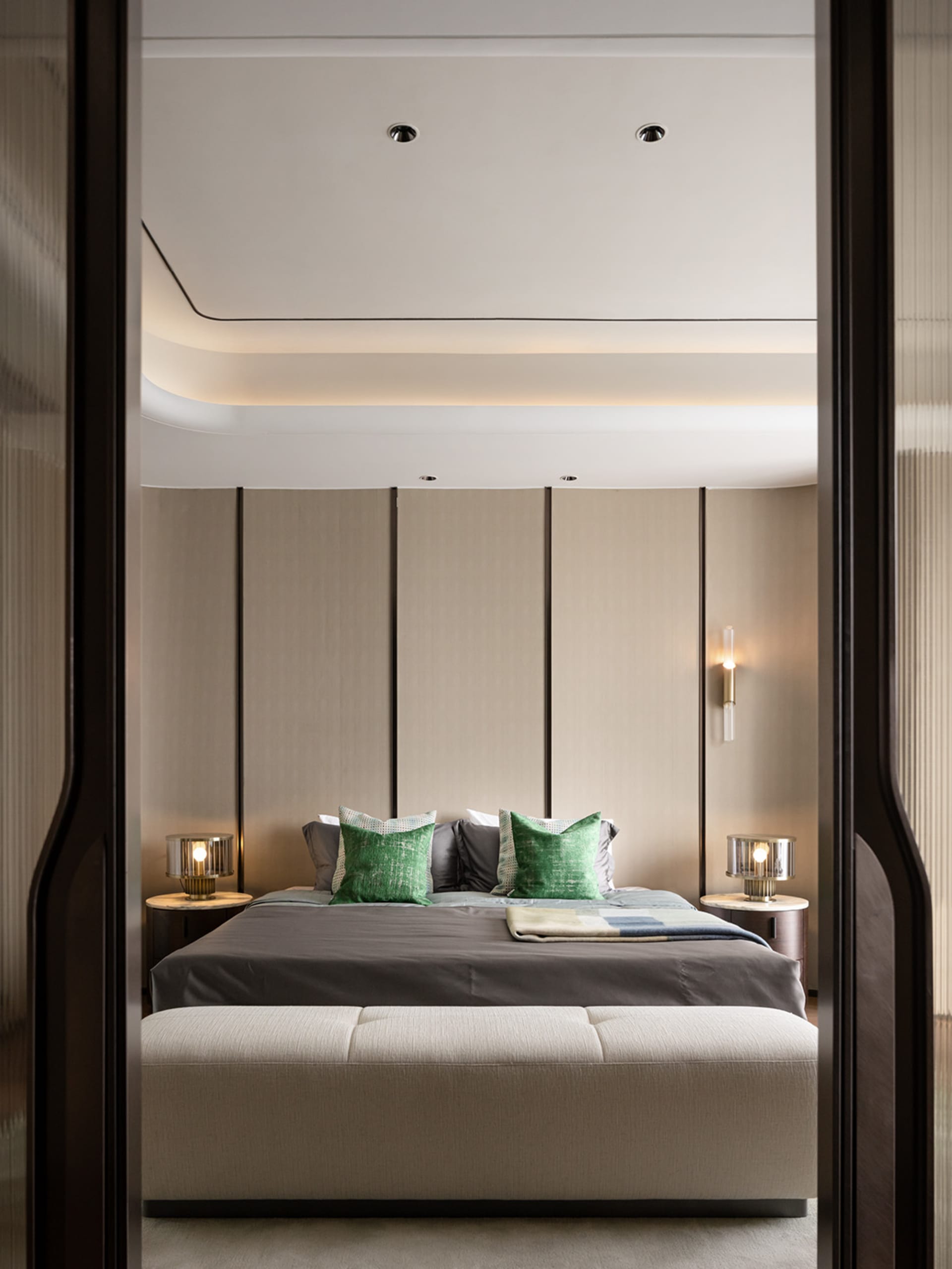 A minimalist bedroom featuring textured fabric on the bed, wooden headboard, and glass bedside lamps.