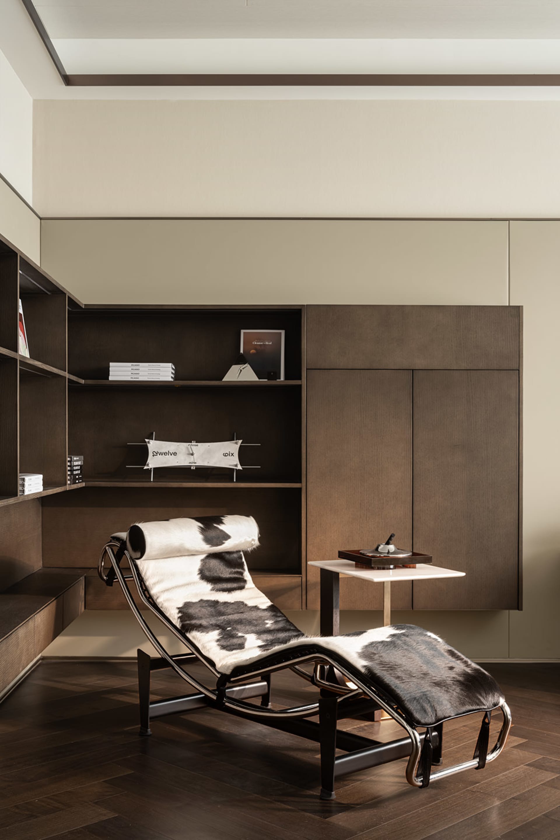 A modern living room with wooden furniture, including a cowhide chaise lounge and a bookshelf.