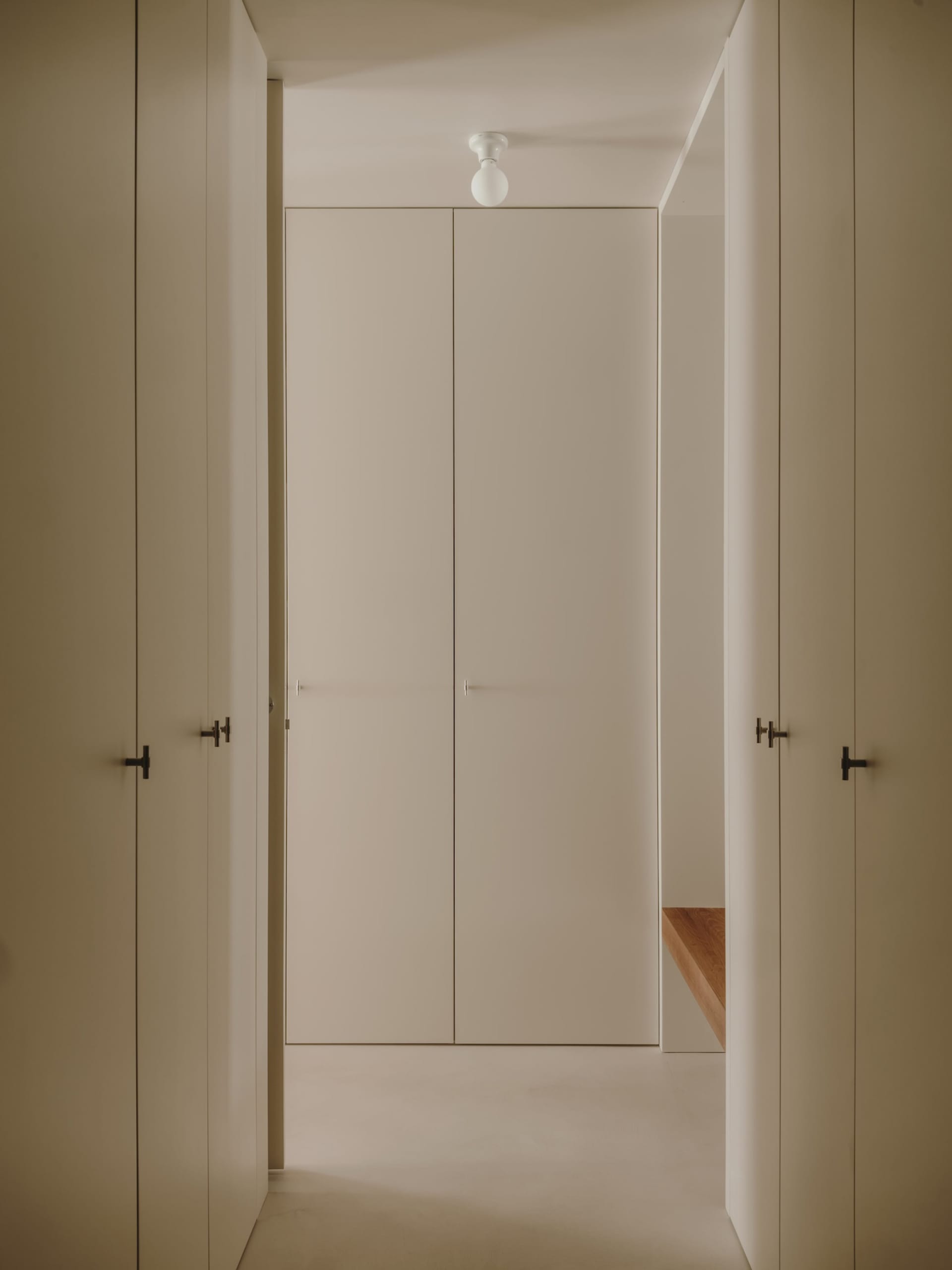 A minimalist hallway with concrete flooring and walls, featuring a central light fixture.