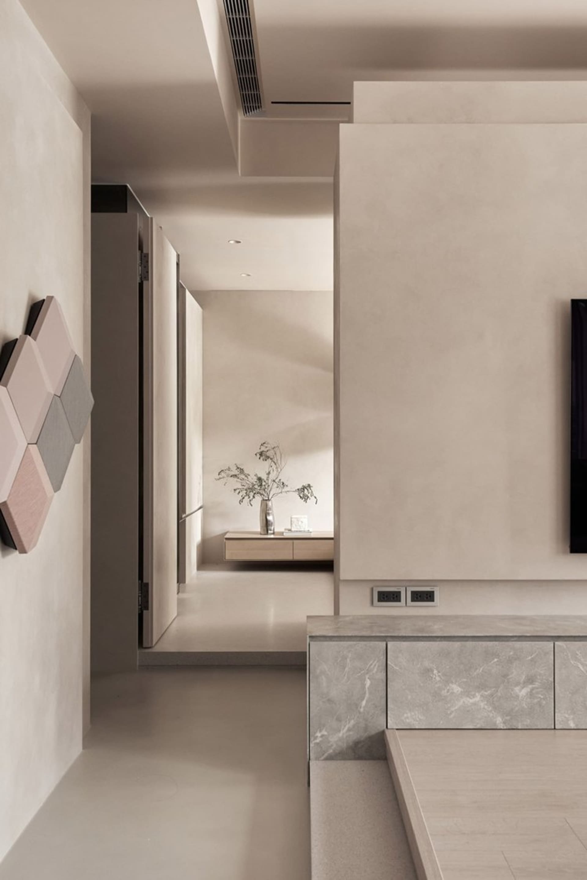 A minimalist living room with concrete walls and floor, featuring a wall-mounted TV and a floating shelf.