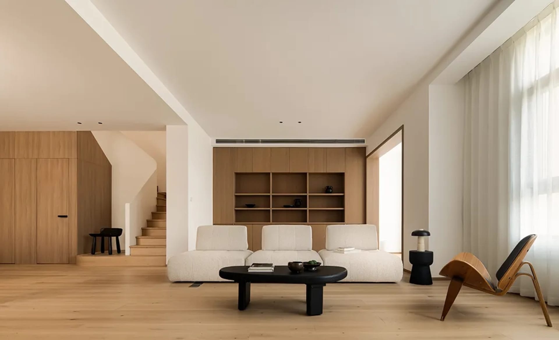 A minimalist living room with wooden elements, including a white sofa, black coffee table, and wooden shelving unit.