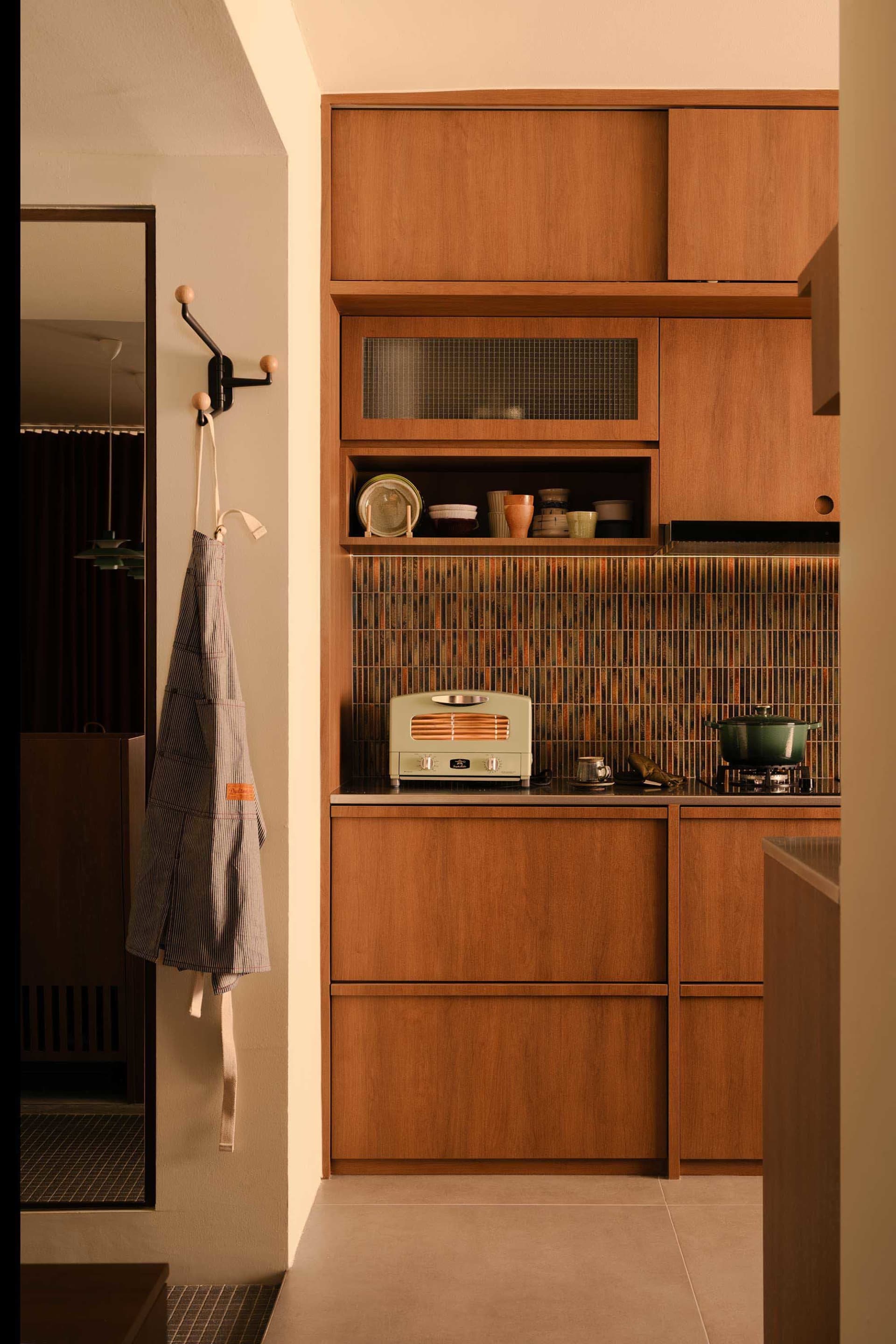 A modern minimalist residential kitchen featuring wooden cabinets and glass mosaic tiles.