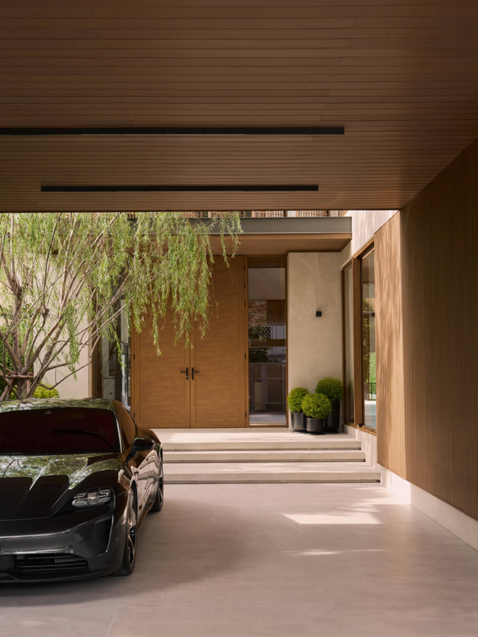 Modern residential entry featuring wooden walls and a black electric car parked outside
