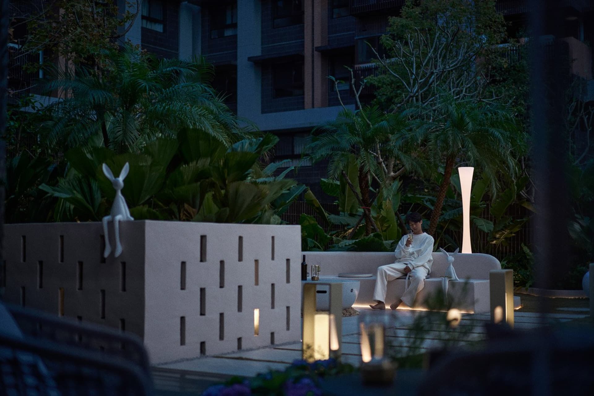 A minimalist living room with a concrete element as the centerpiece, surrounded by lush greenery and modern furniture.