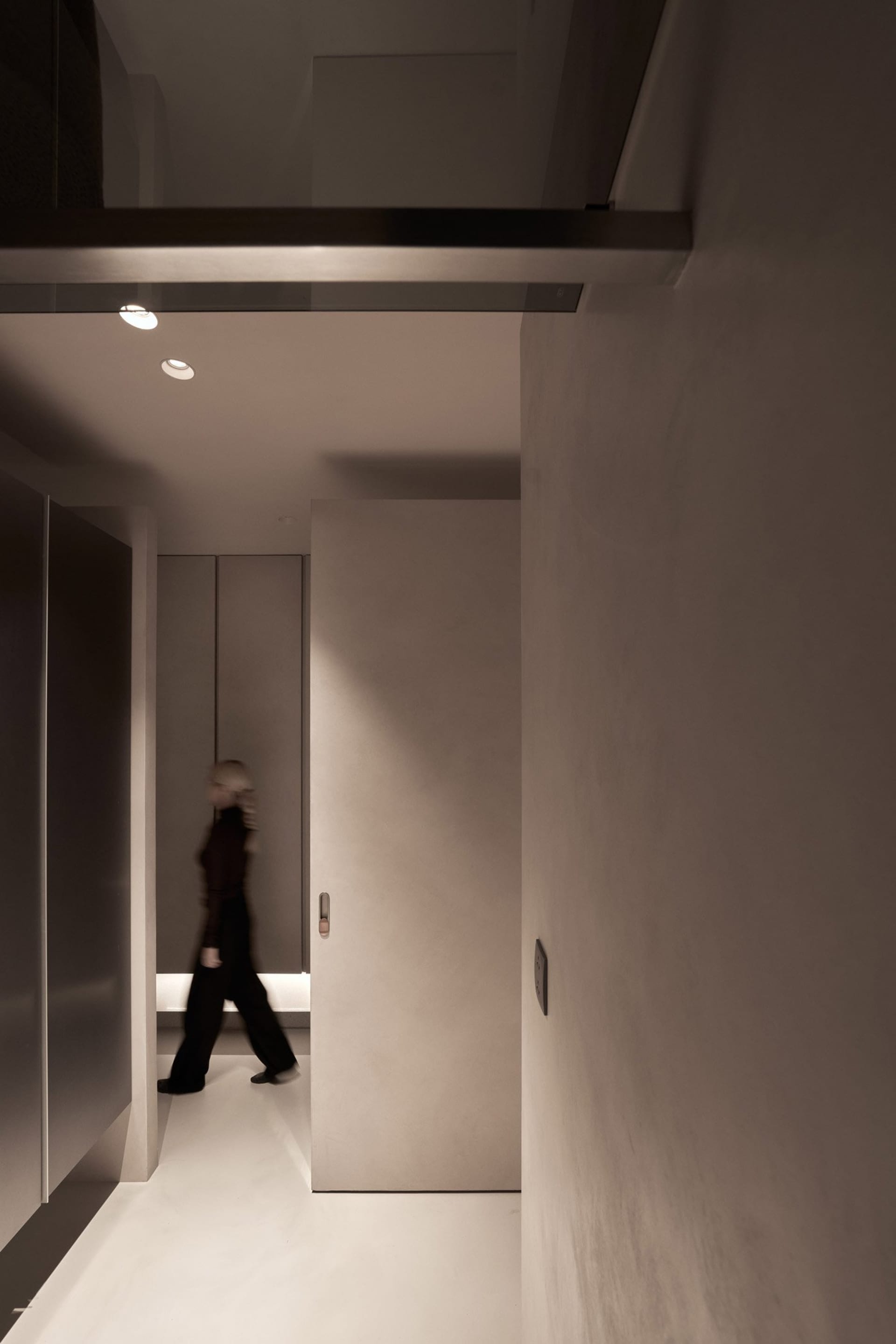 A minimalist hallway with a concrete floor, viewed from the side, featuring subtle lighting.
