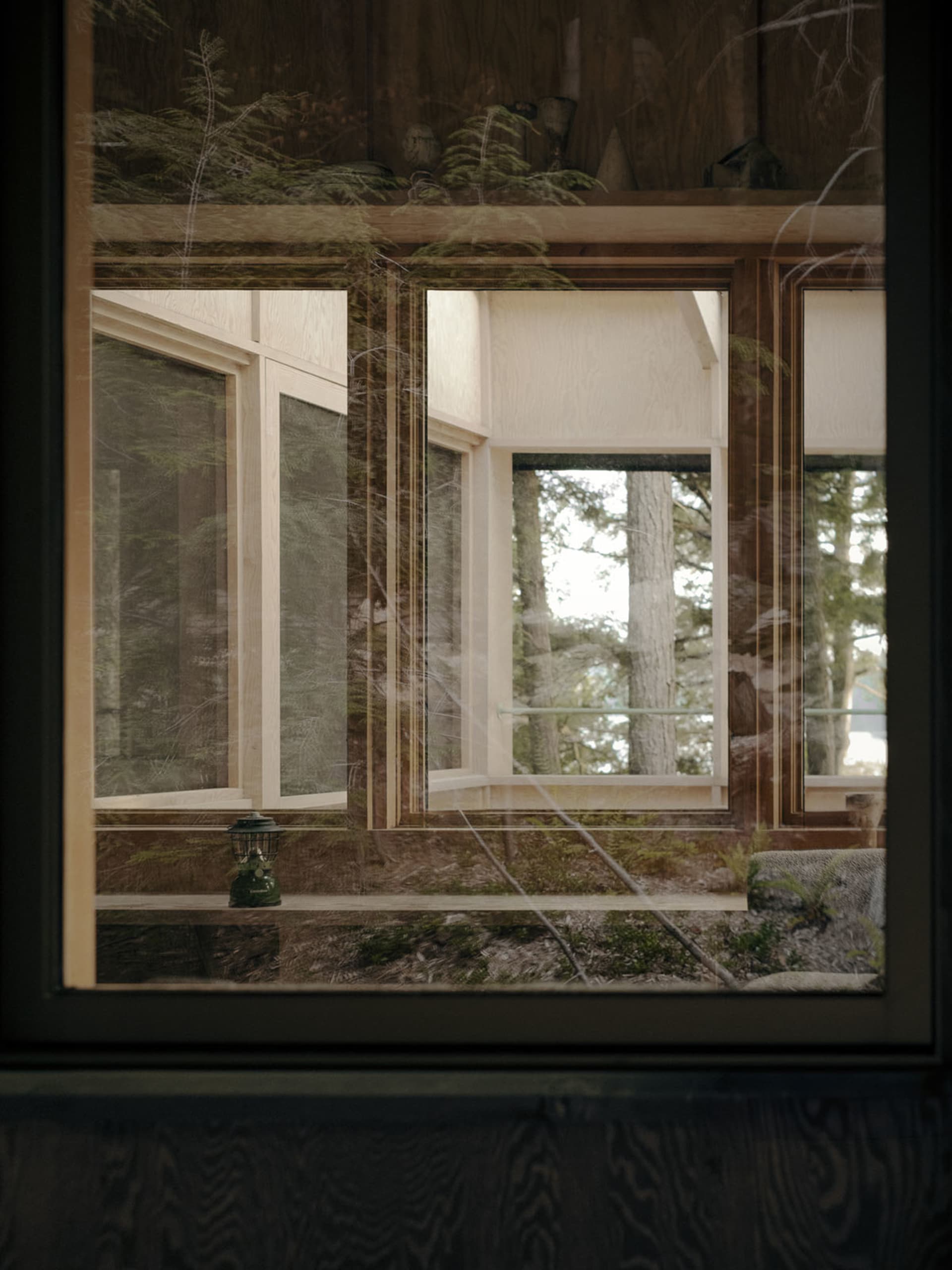 A modern interior space with a large window made of wood, looking out into a forested area.
