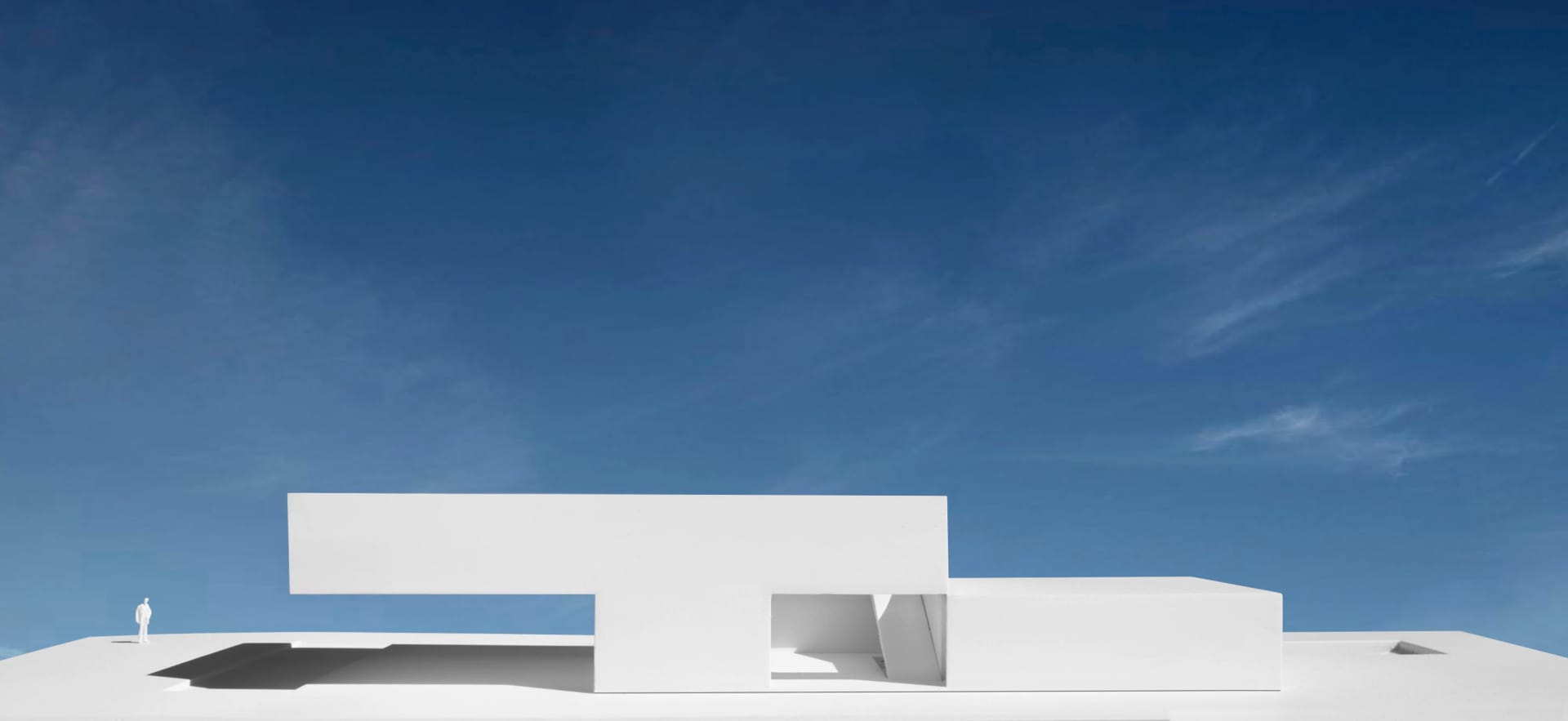 A minimalist white concrete building against a clear blue sky.