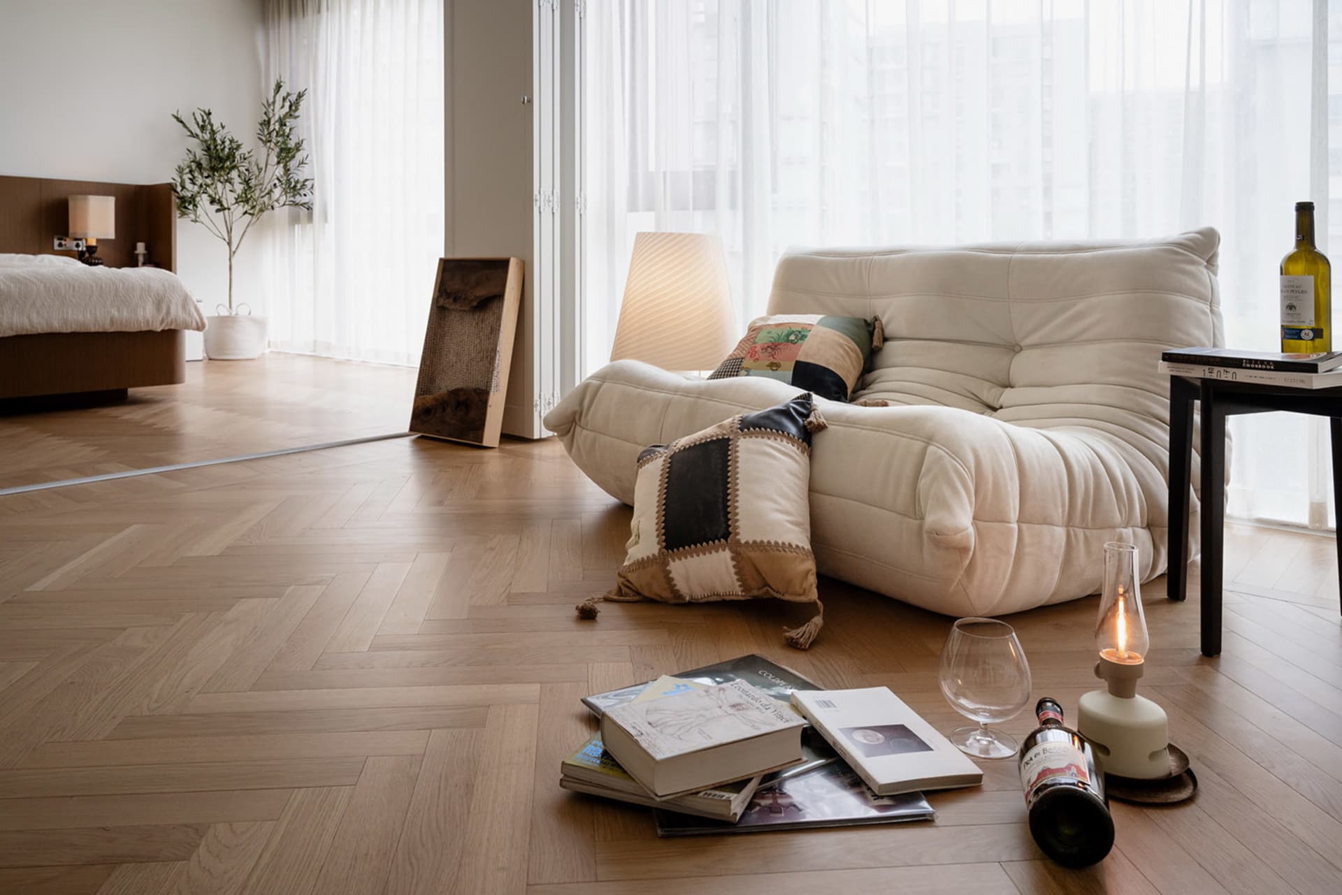 Modern interior design featuring a cozy white sofa, books, and wine glass on a wooden floor.