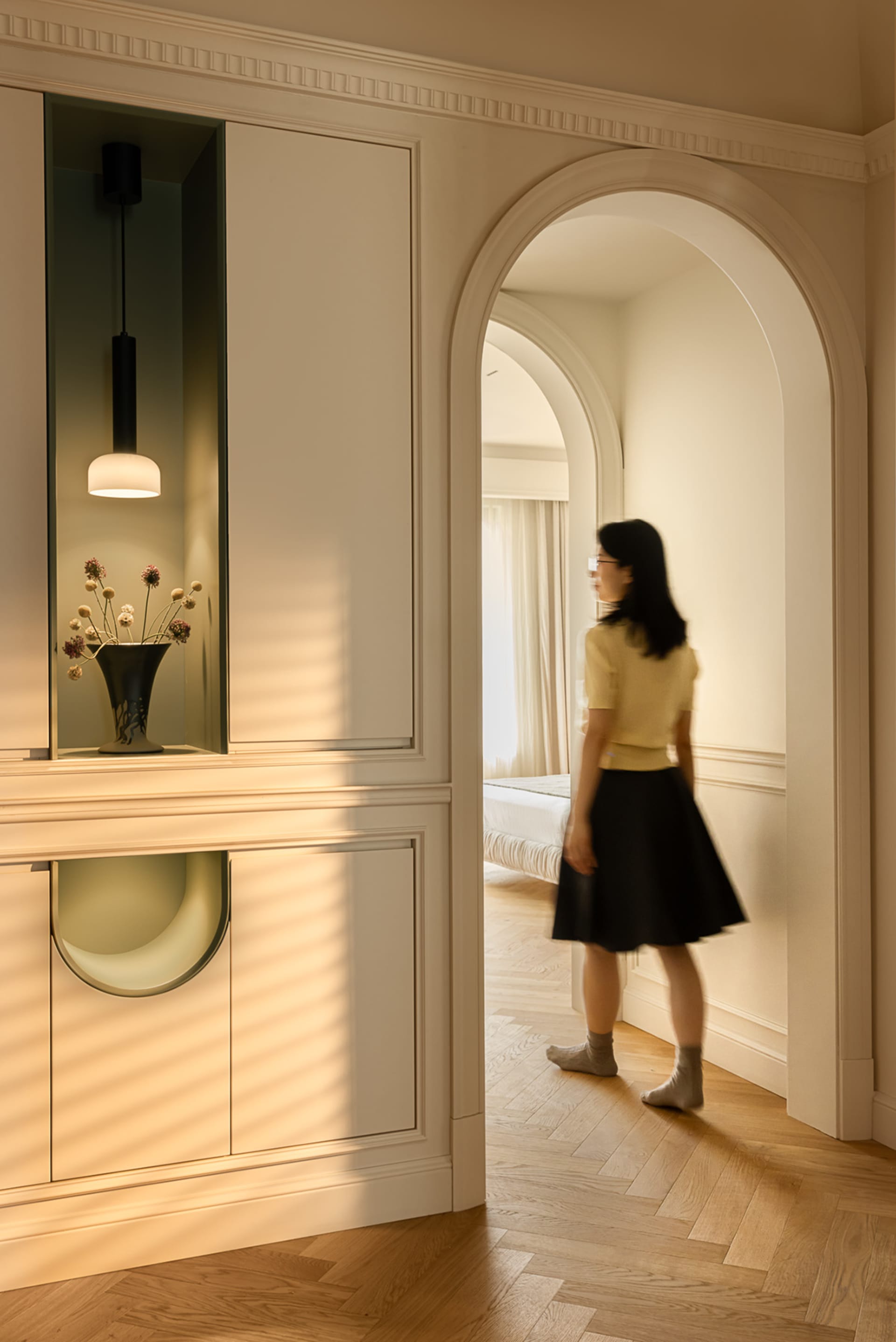 A minimalist modern bedroom with wooden floors, a bed, and a person standing in the doorway.