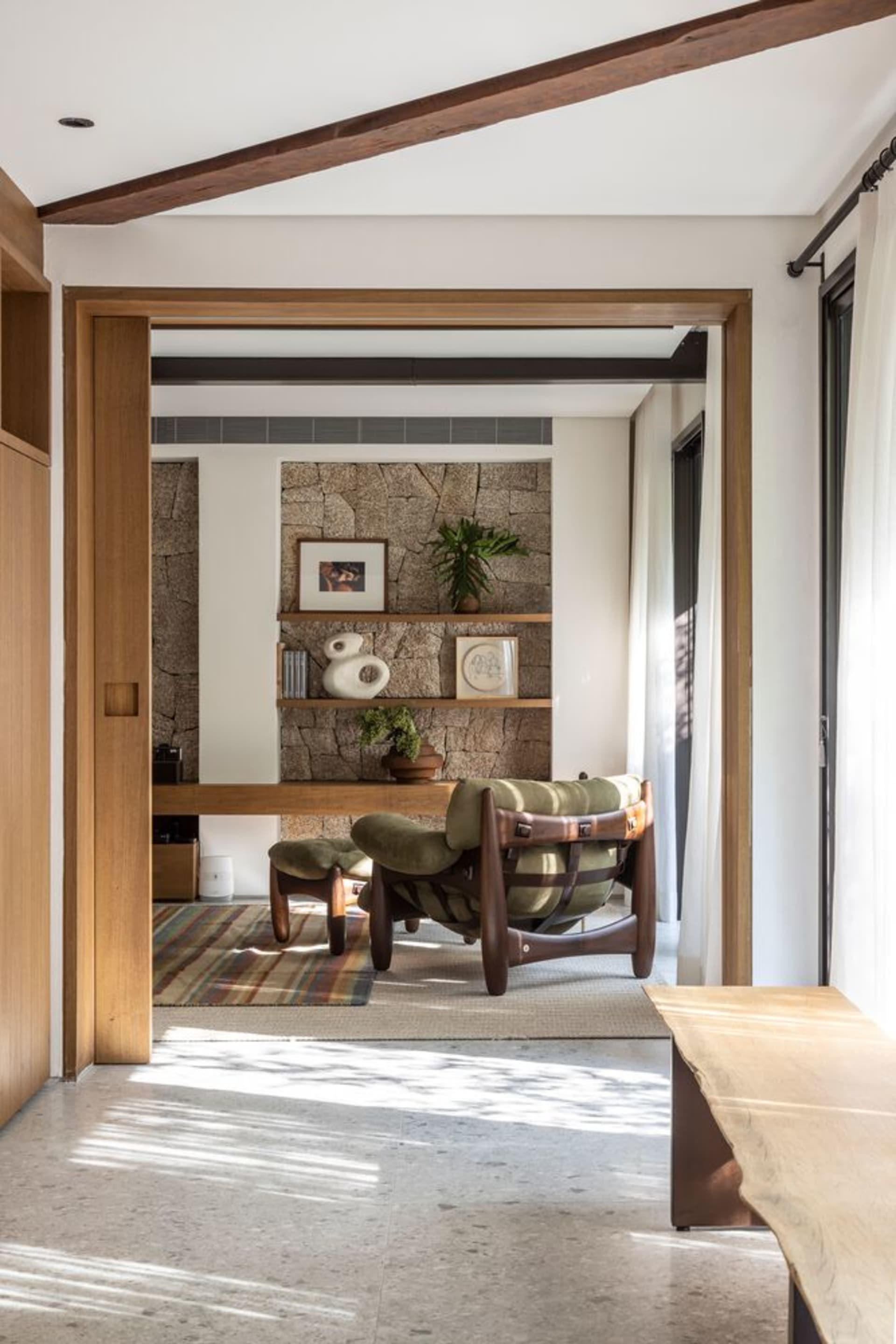 Modern minimalist living room with wooden furniture and a stone wall.