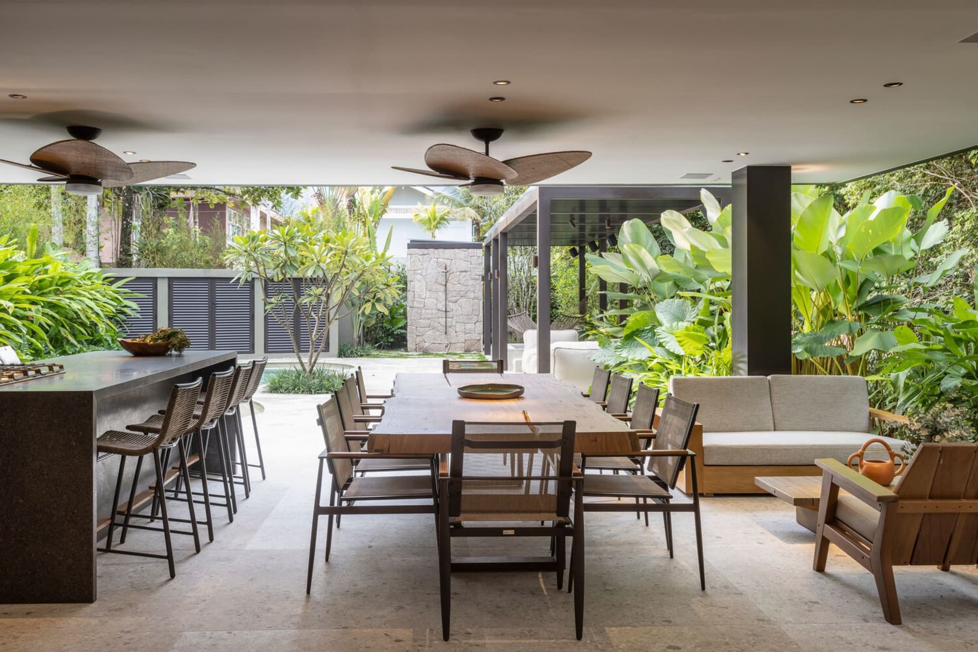 Modern outdoor living space with a wooden dining table, concrete floor, and lush plants.