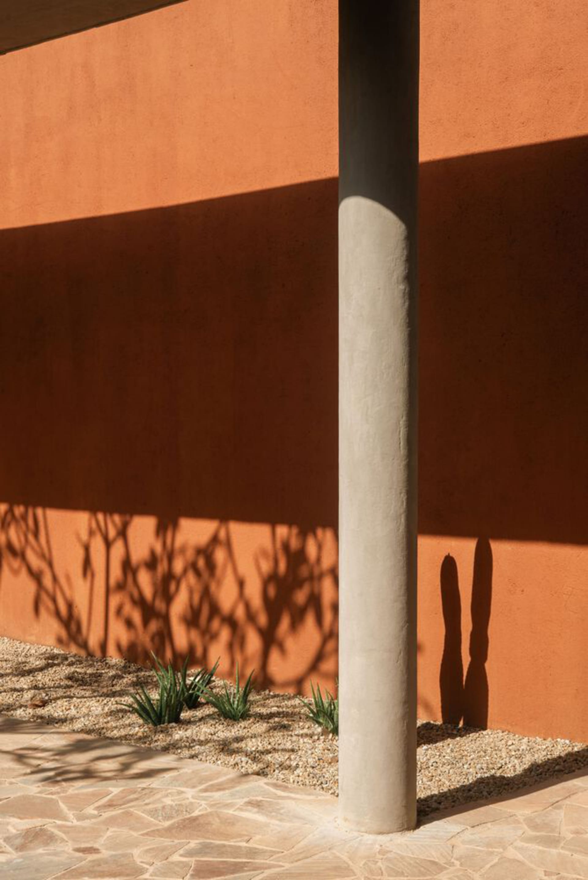 A minimalist exterior design featuring a concrete column casting a shadow on a textured wall.