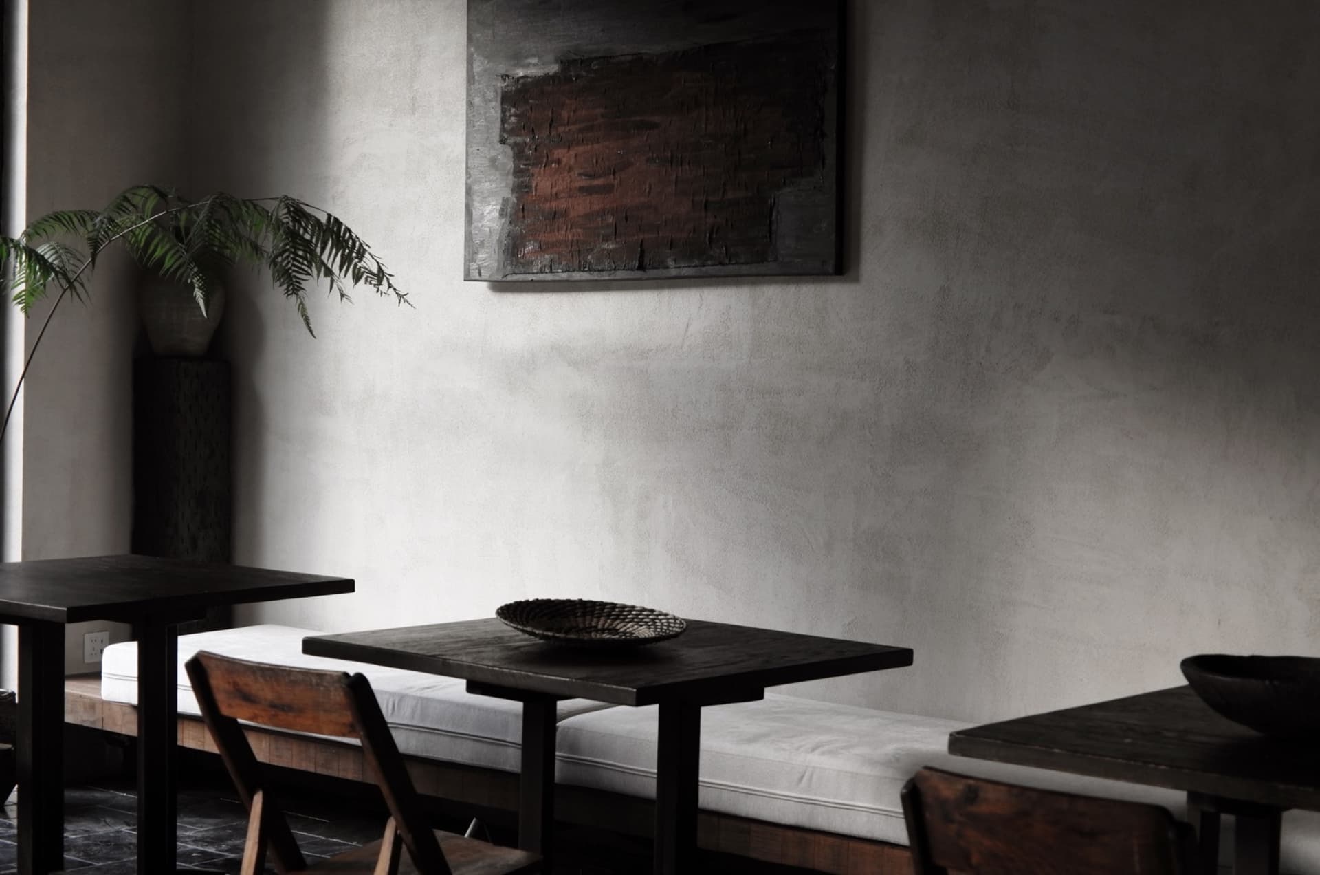 A minimalist restaurant interior featuring concrete walls and wooden furniture.
