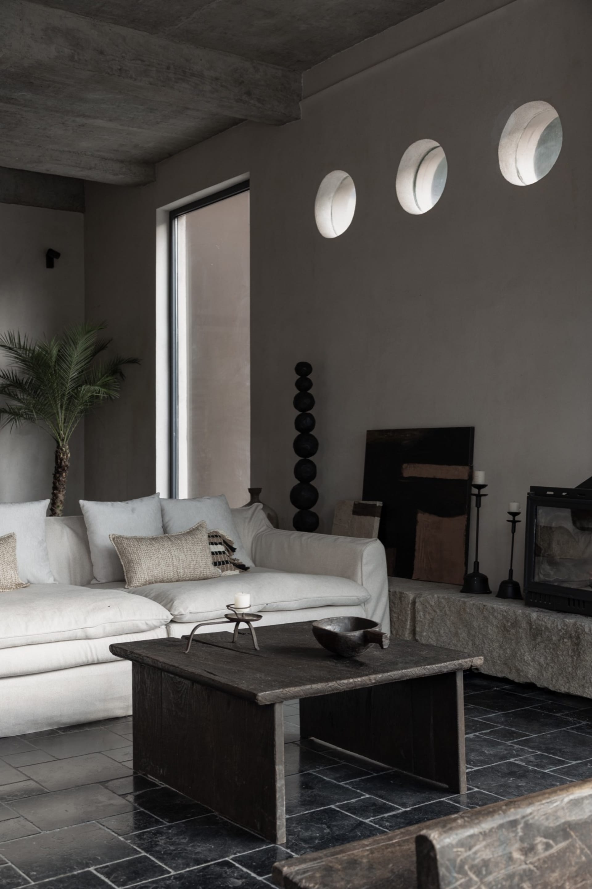 A modern living room with a minimalist design, featuring a concrete floor and walls, large windows, and a cozy seating area.