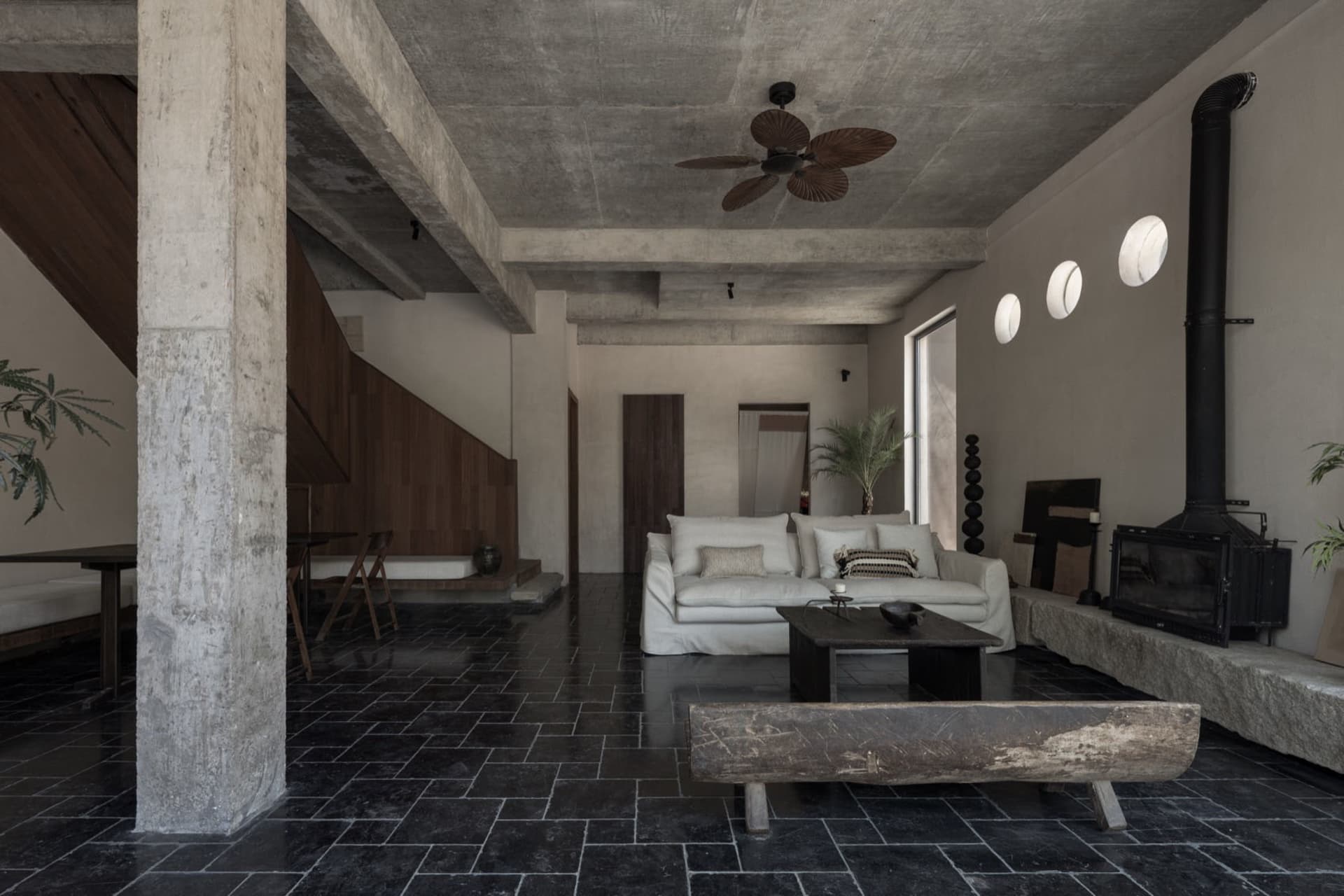 Modern minimalist living room with exposed concrete ceiling and black tiled floor, featuring a white sofa and a wooden coffee