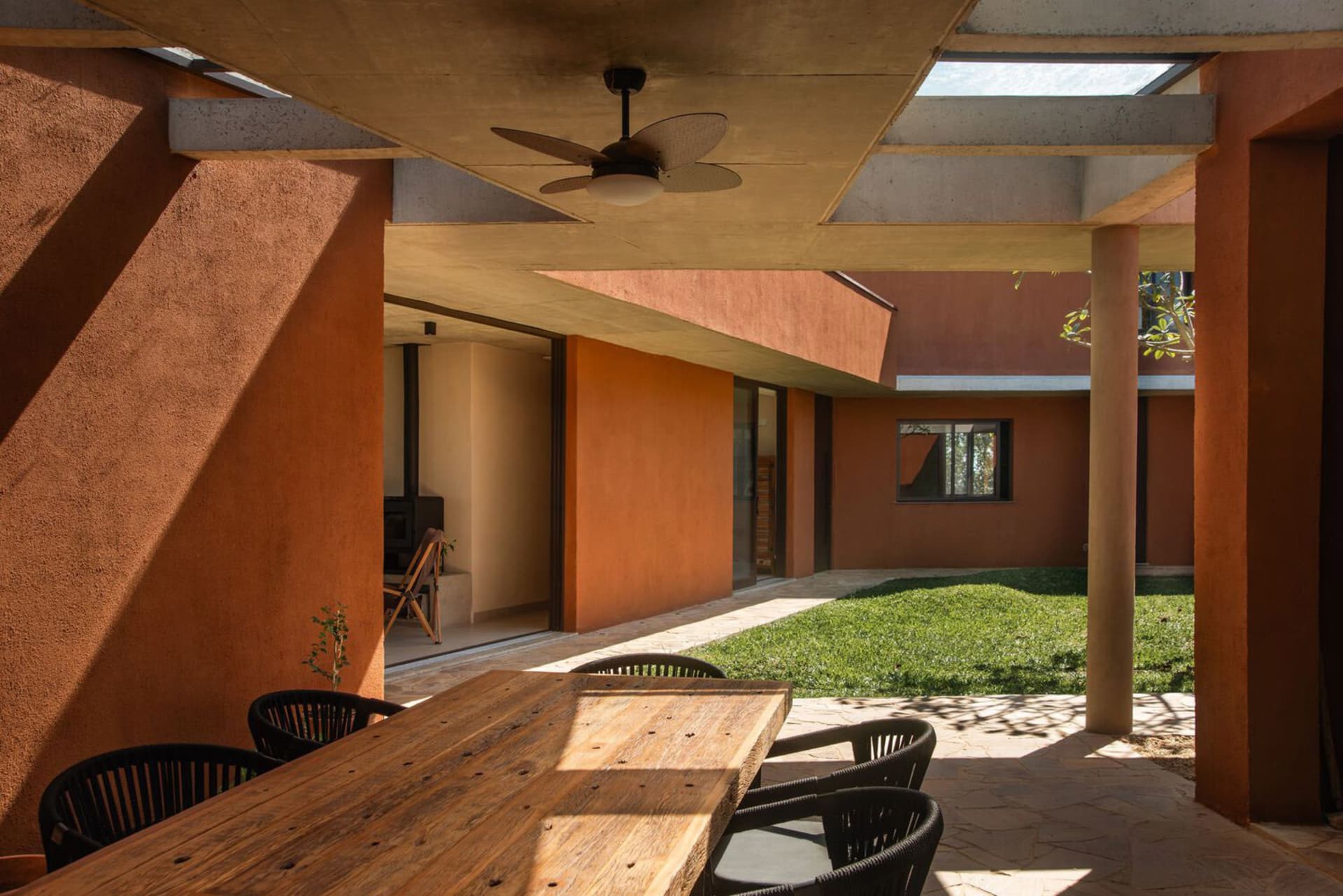 A modern porch with wooden table, concrete floor, and a view of a green lawn and house interior.