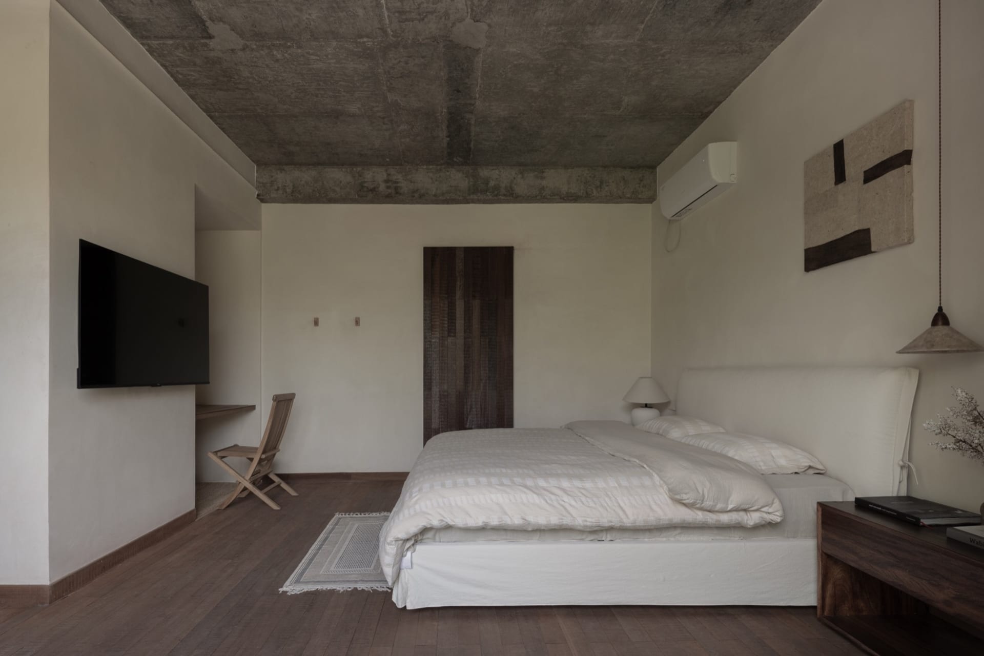 A modern industrial-style bedroom with concrete elements, featuring a single bed with white bedding and a minimalist design.