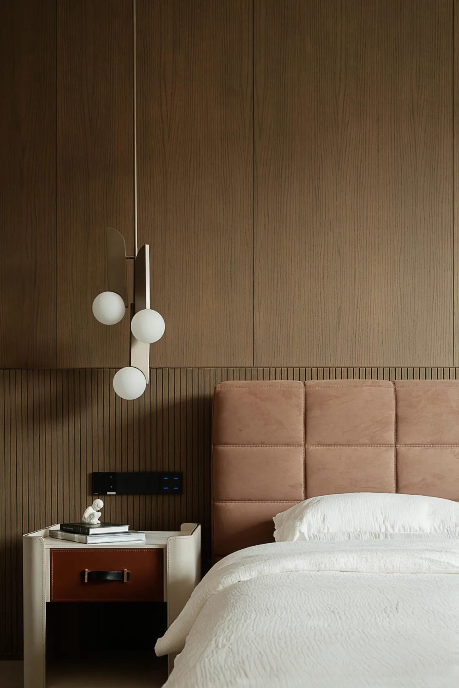 A minimalist bedroom featuring a textured wood wall and headboard, with a white bedspread and a modern light fixture.