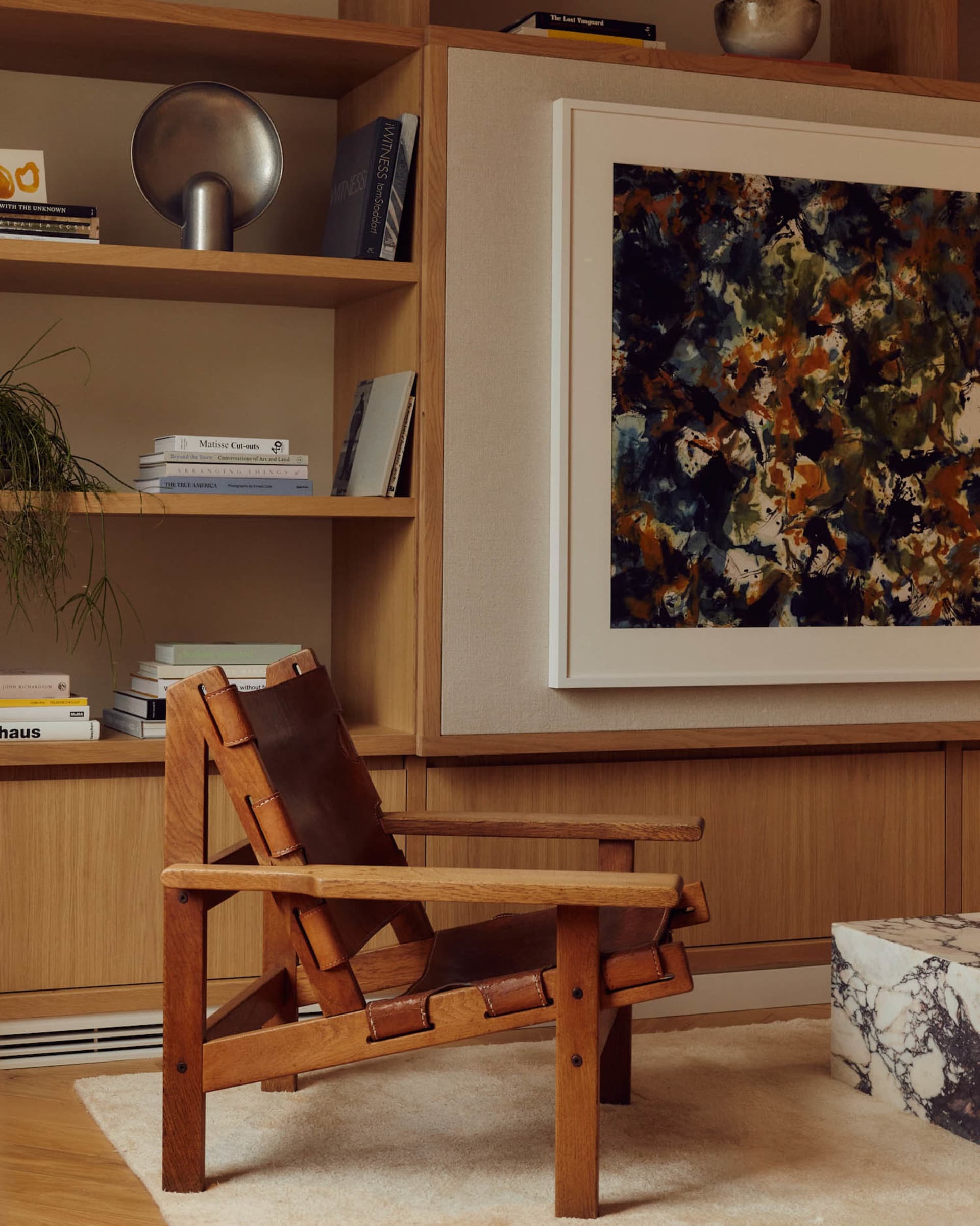 A modern living room featuring a wooden armchair, abstract art, and a bookshelf with books and decorative items.