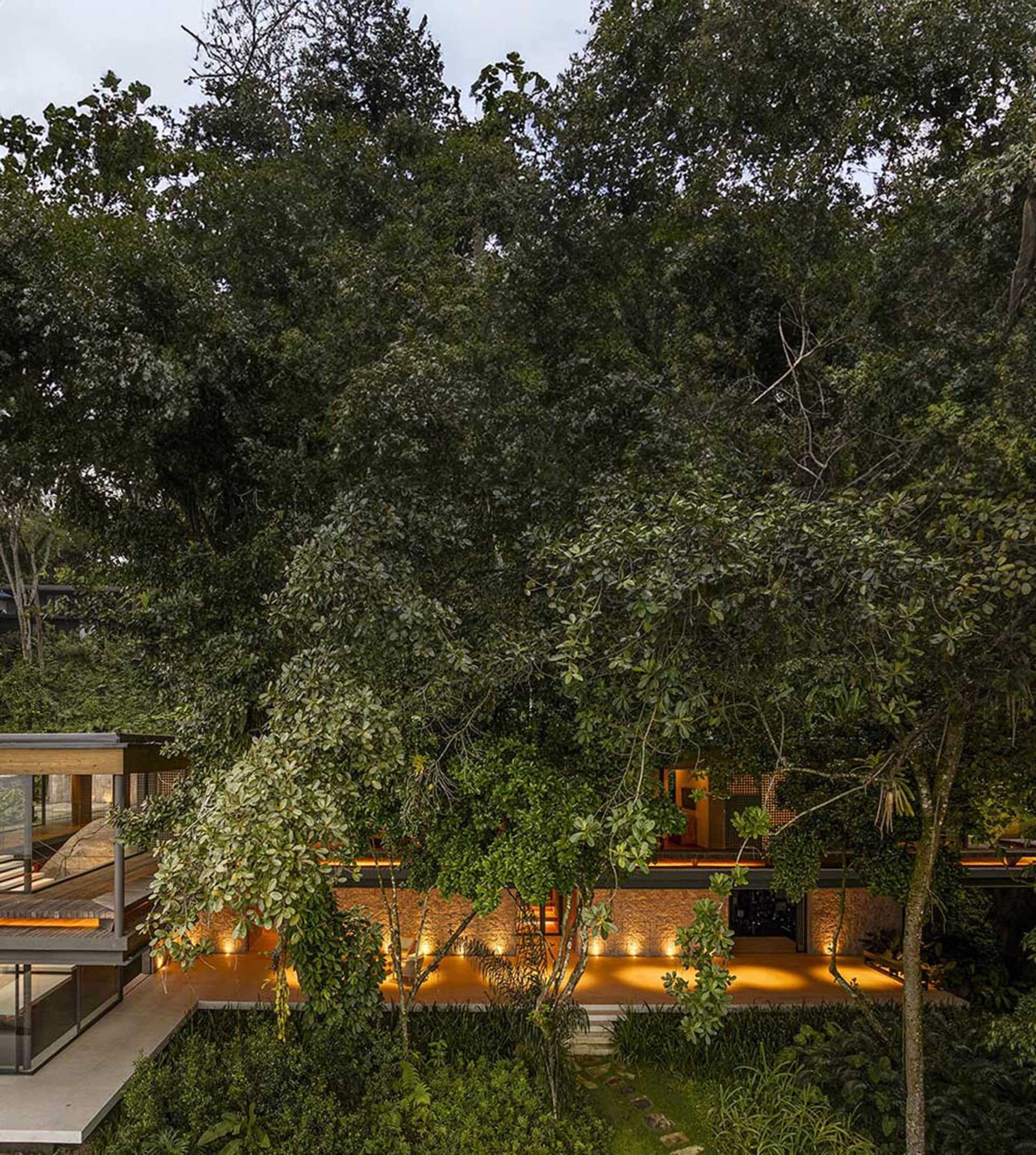 A modern residential house with wooden exterior and concrete accents surrounded by lush greenery.