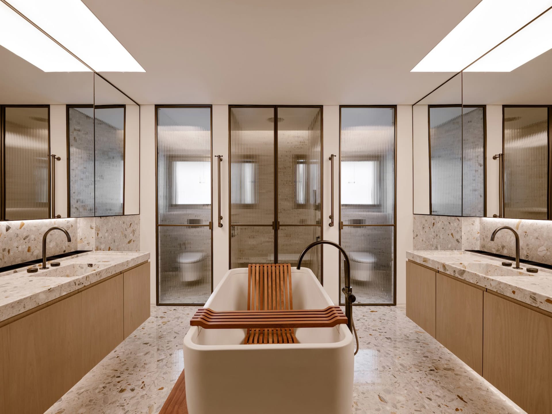 Modern minimalist bathroom featuring a free-standing white bathtub with a wooden tray, surrounded by terrazzo marble countert
